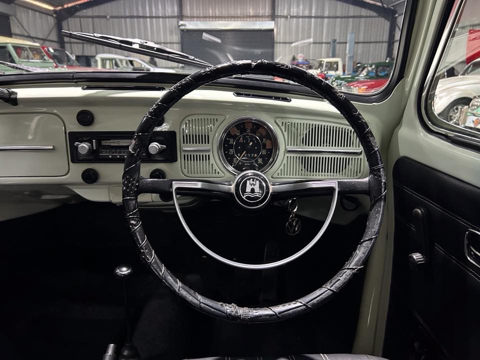 Interior of a vintage car showing a circular steering wheel, chrome accents, and a two-tone dashboard with a central speedometer.