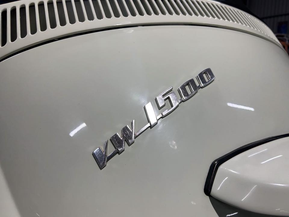 Close-up of a vintage car’s side with a chrome 'VW 1500' badge on a cream-colored body, diagonally mounted.