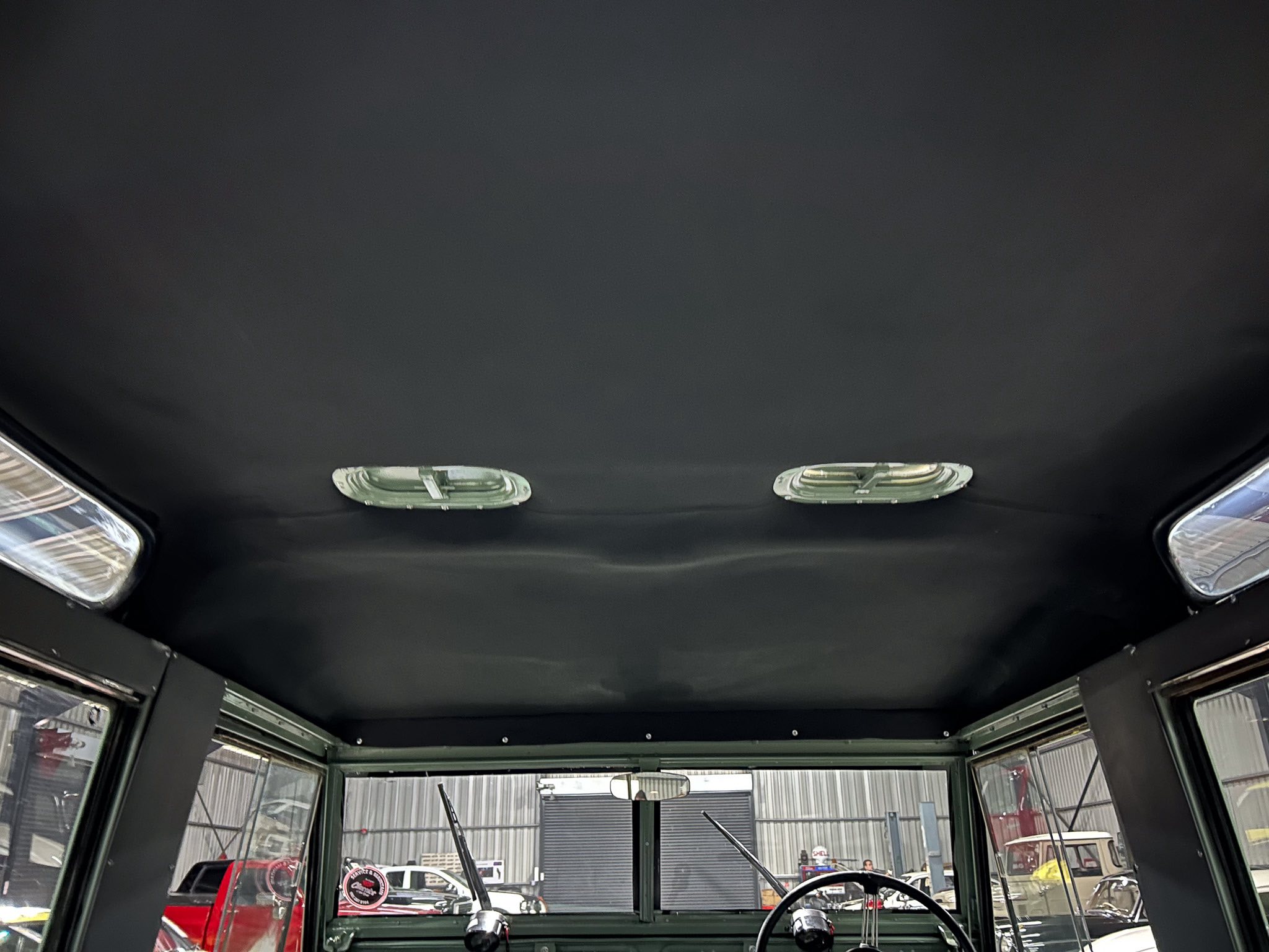 Interior of a vintage car cabin seen from the rear, with a black headliner and two overhead lights