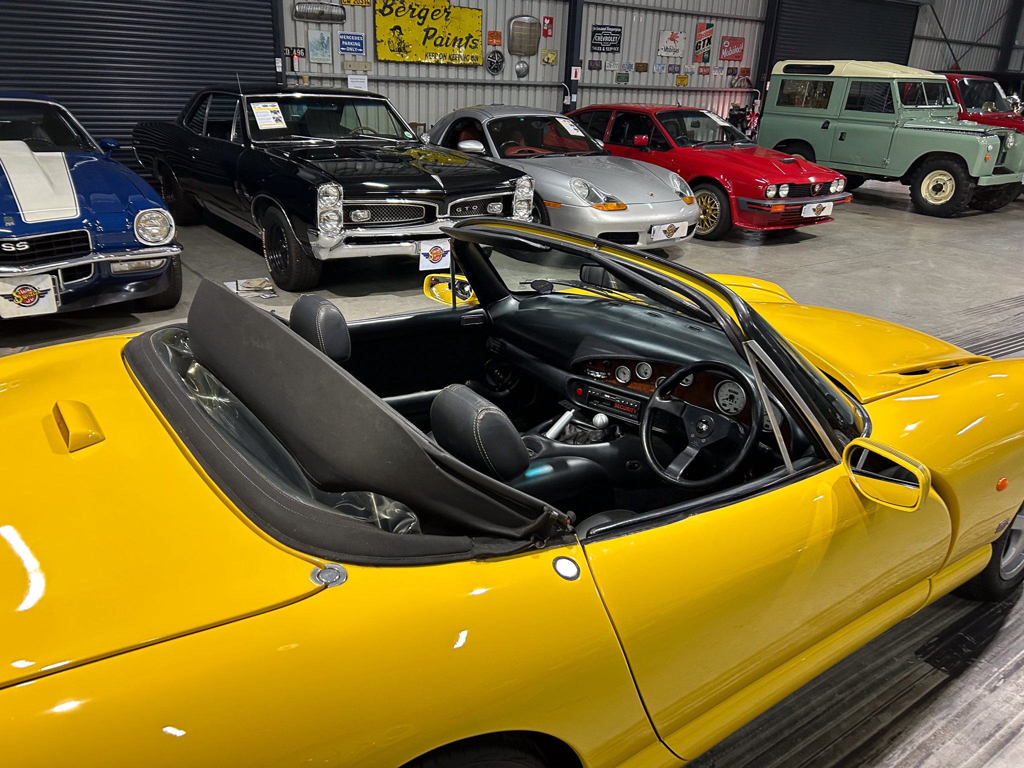 Yellow convertible in the foreground with black interior inside a classic car showroom, other vintage cars lined up in the background