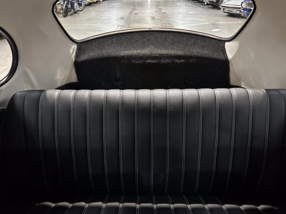 Back seat of a black leather car interior with white stitching and a rear window view of a showroom or garage outside