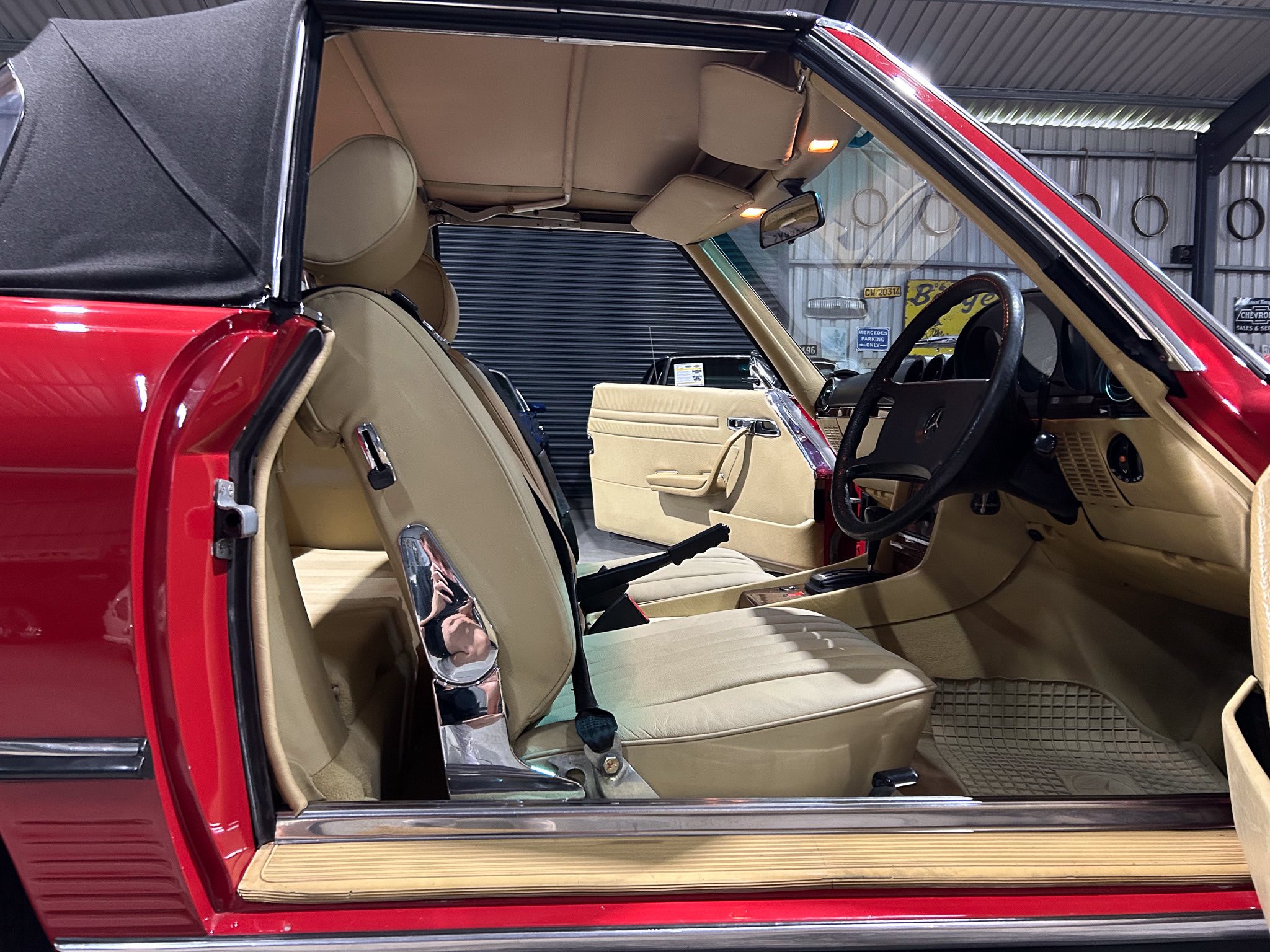 Red vintage convertible with tan leather interior; open driver's door, showing steering wheel and dashboard in a showroom.