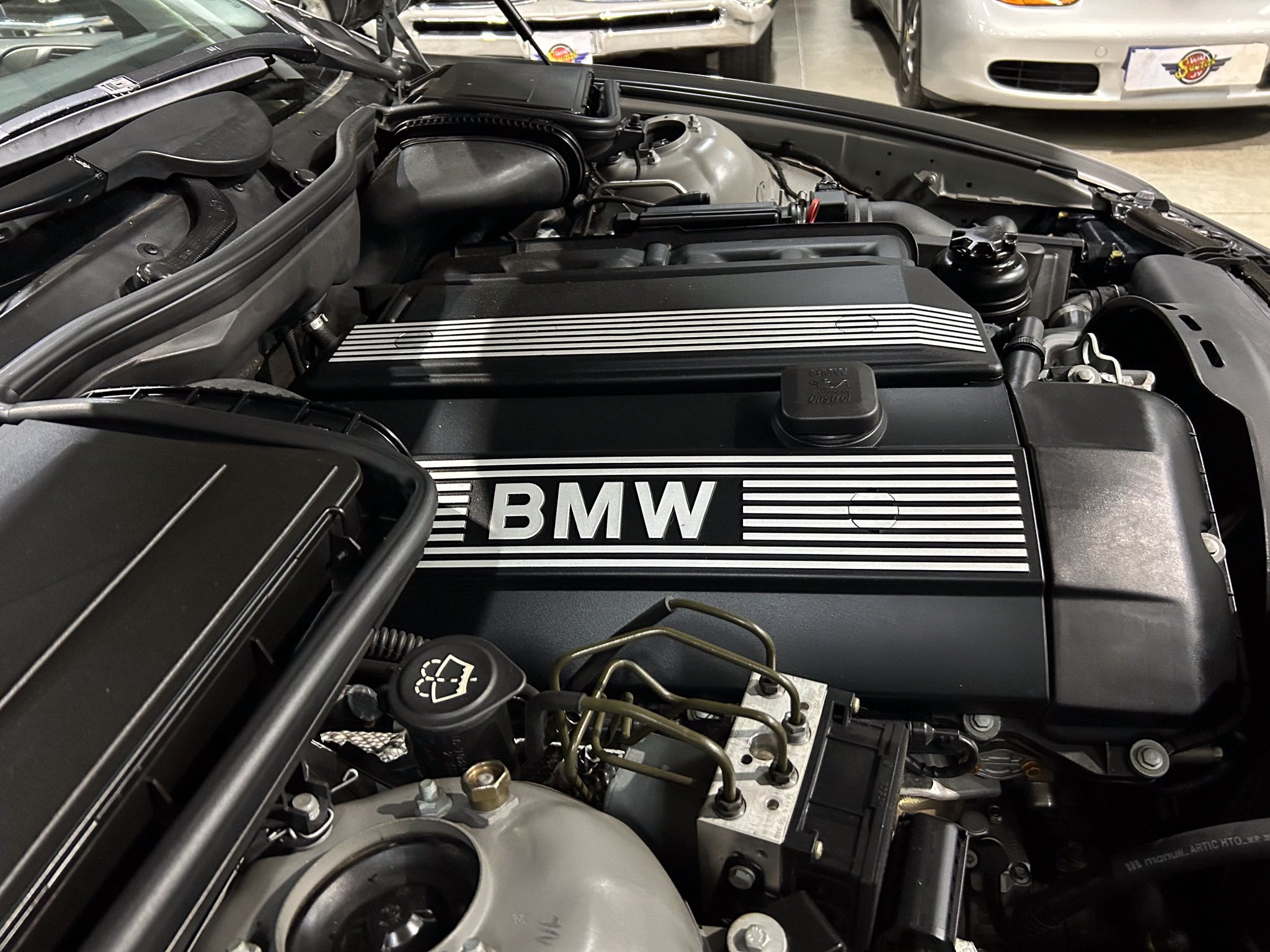 BMW engine bay with a prominent striped engine cover and exposed components under the hood in a showroom setting