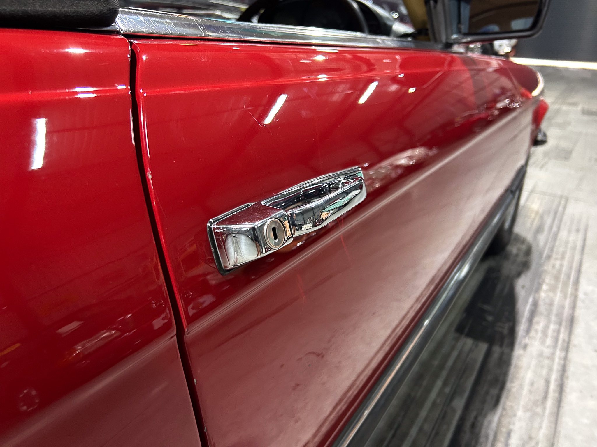 Close-up of a glossy red car door with chrome trim and reflections.