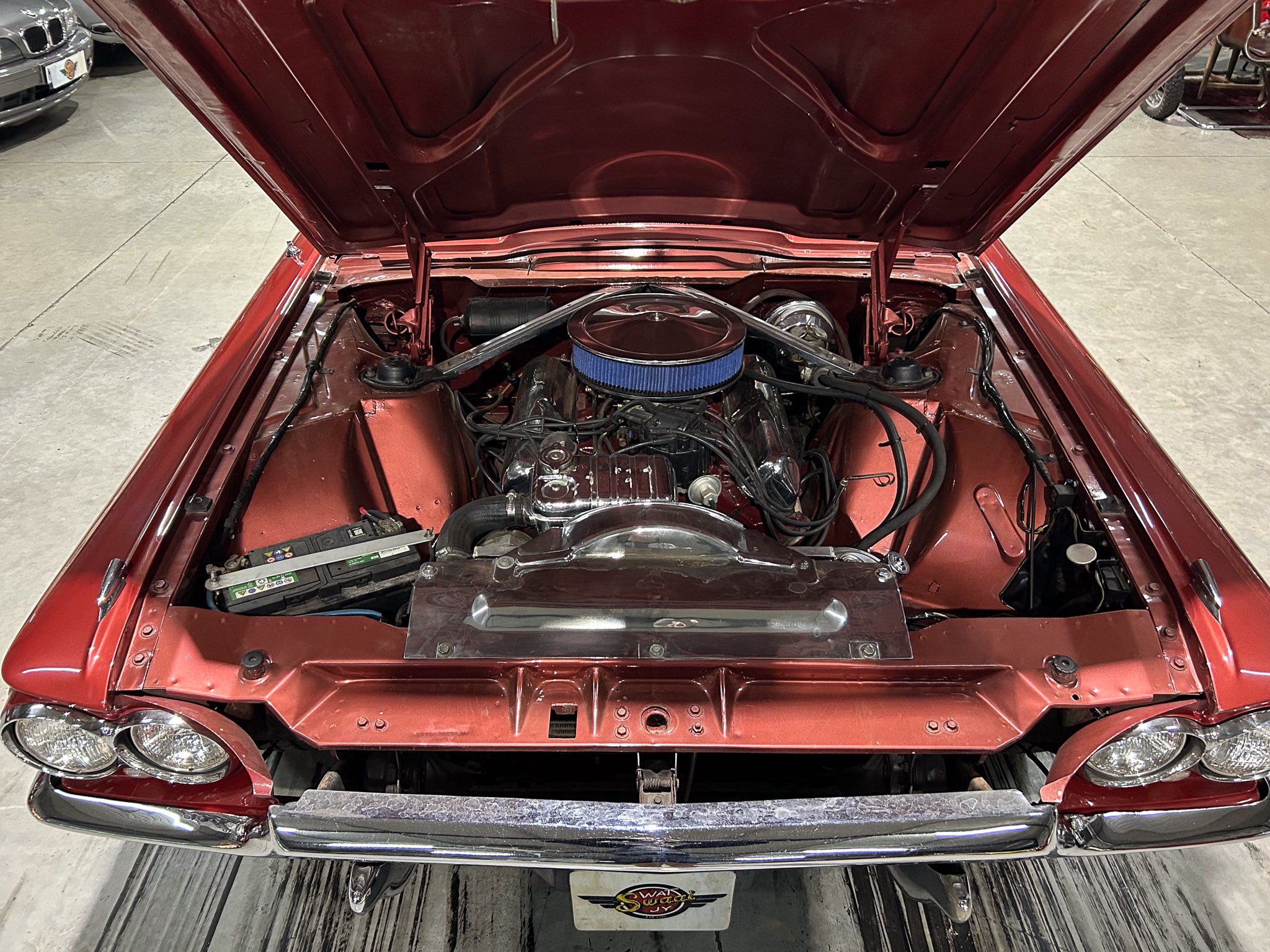 Front view of a classic red car with its hood open, exposing a clean engine bay and blue air filter.
