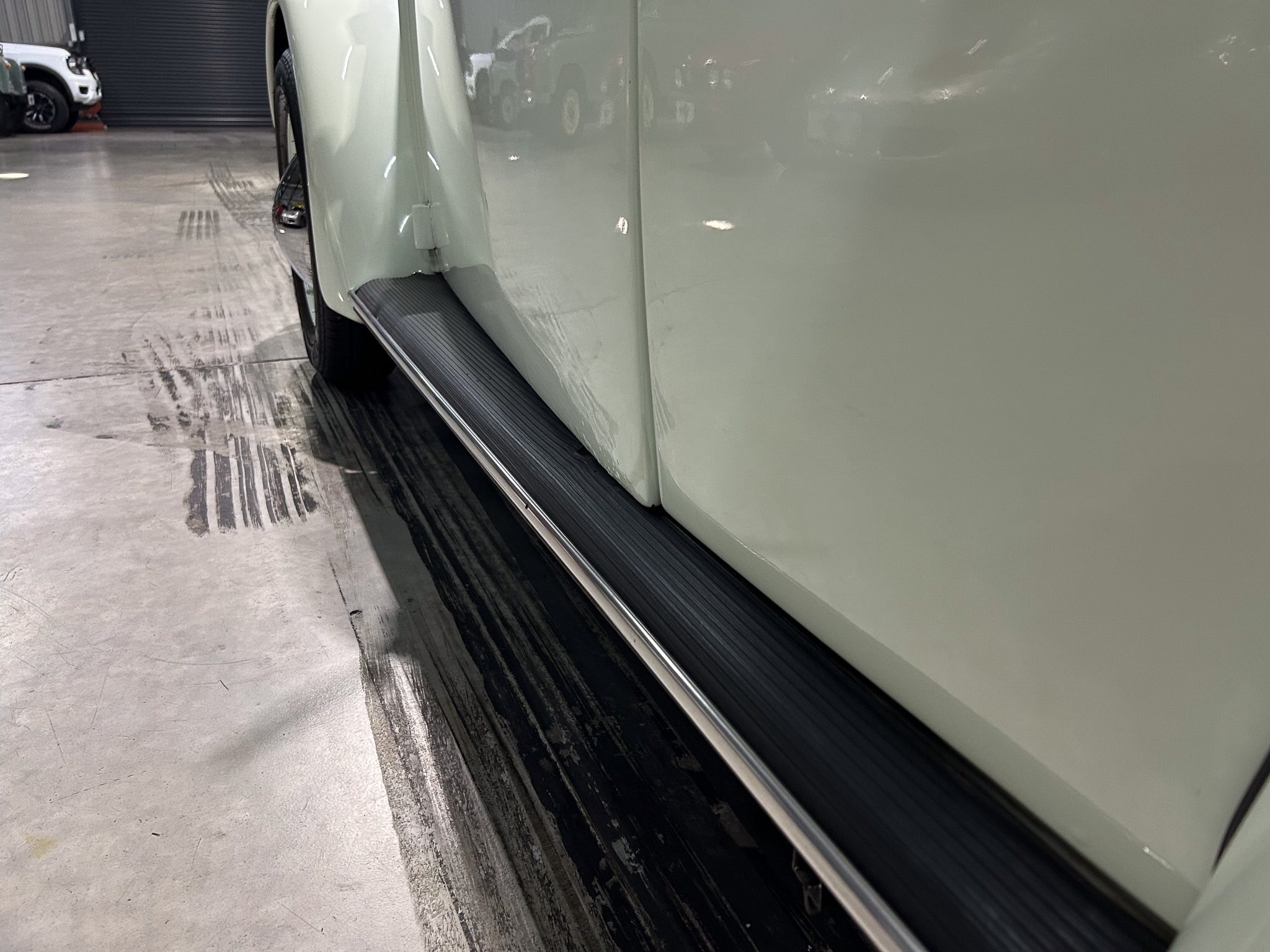 Close-up of a pale green car’s side with a black running board inside a garage.