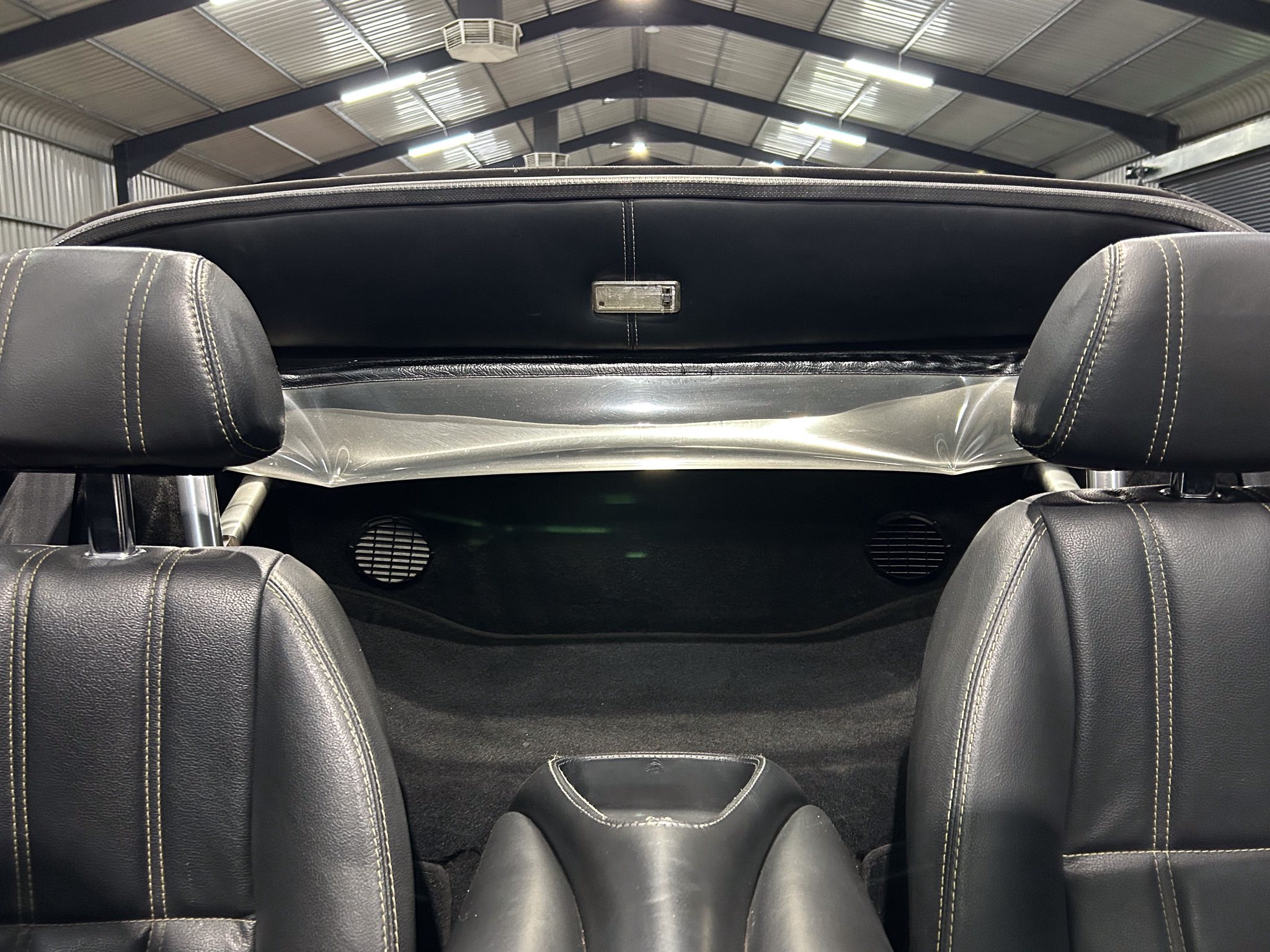 View from inside a black leather car with an open convertible top and a warehouse ceiling visible overhead.