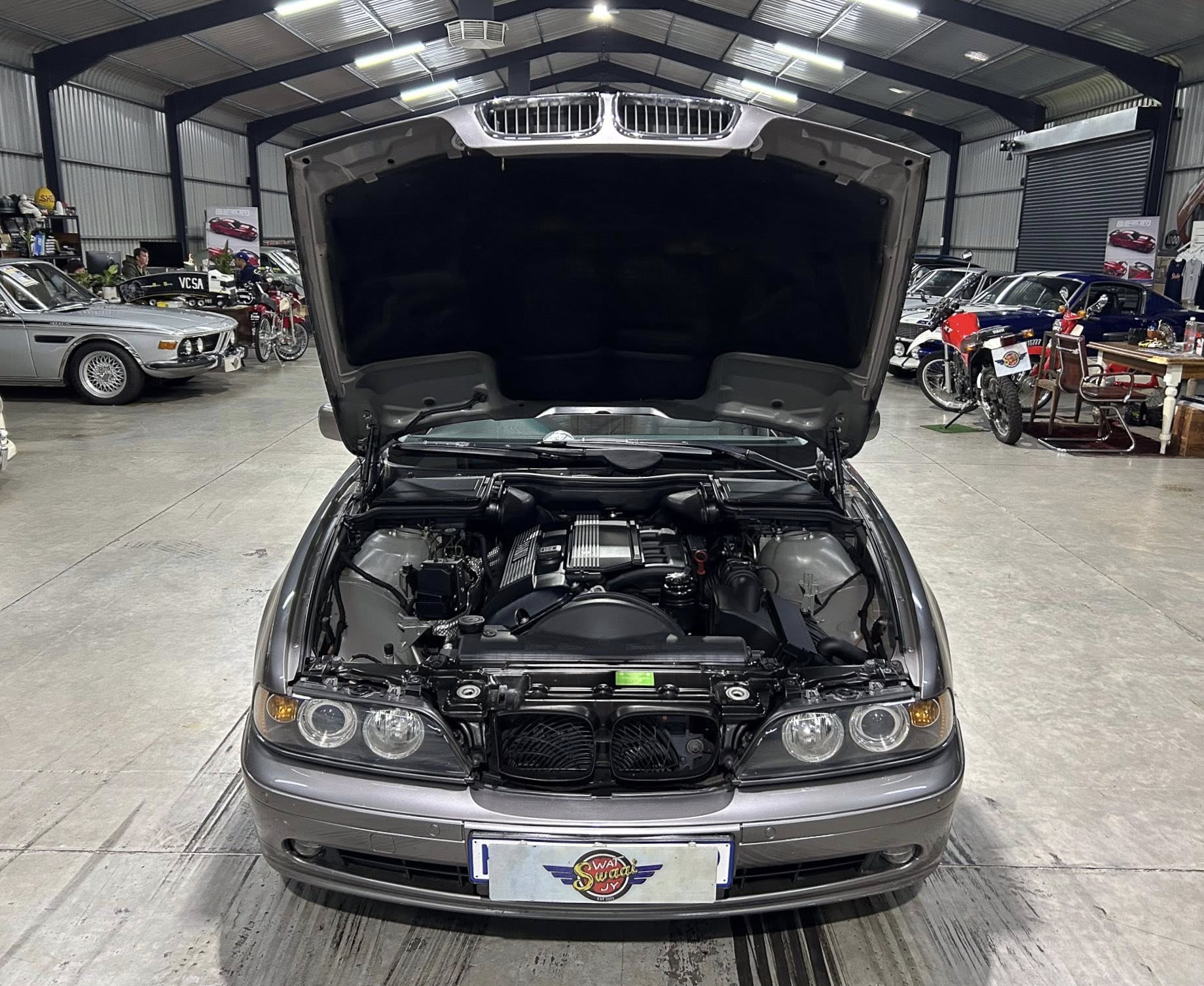Front view of a gray car with its hood raised inside a showroom, exposing the engine area.