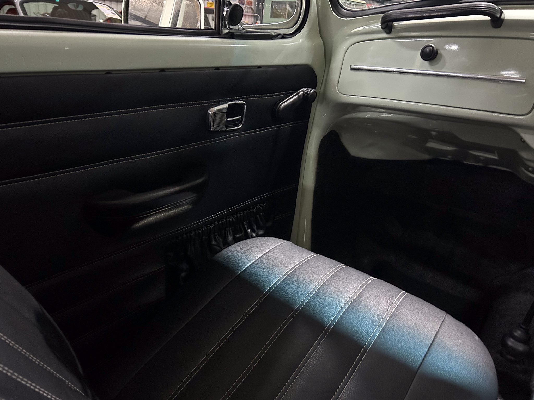 Vintage car interior: black leather door panel with white stitching, chrome door latch, and window crank.