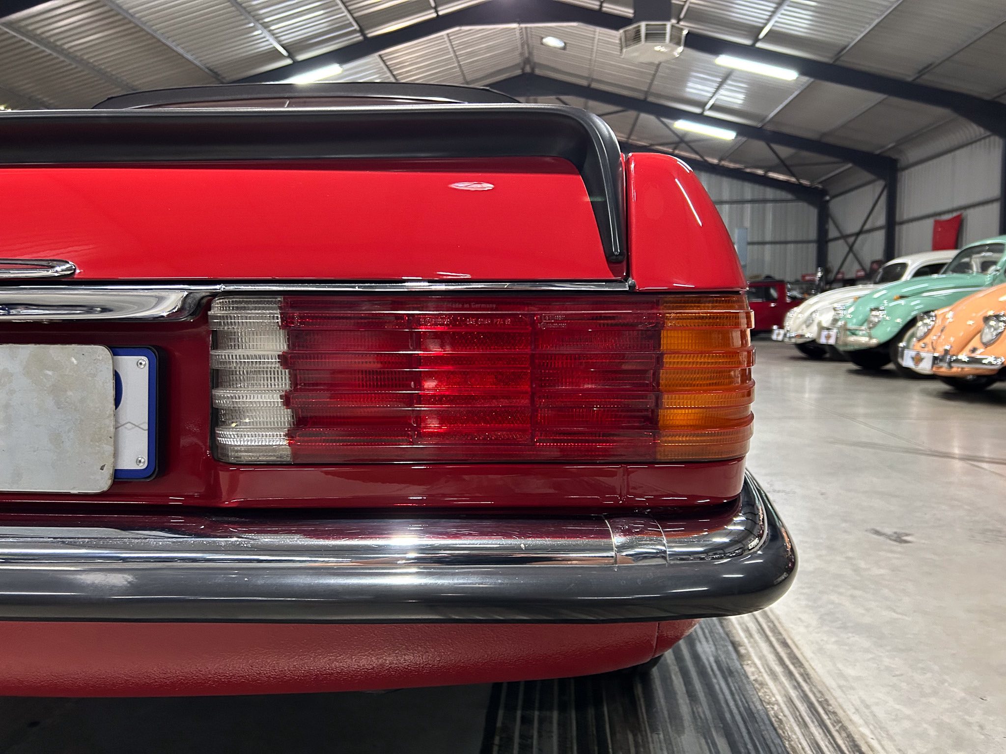 Close-up of a red vintage car's rear end with taillight assembly in a showroom or garage, other classic cars visible in the background