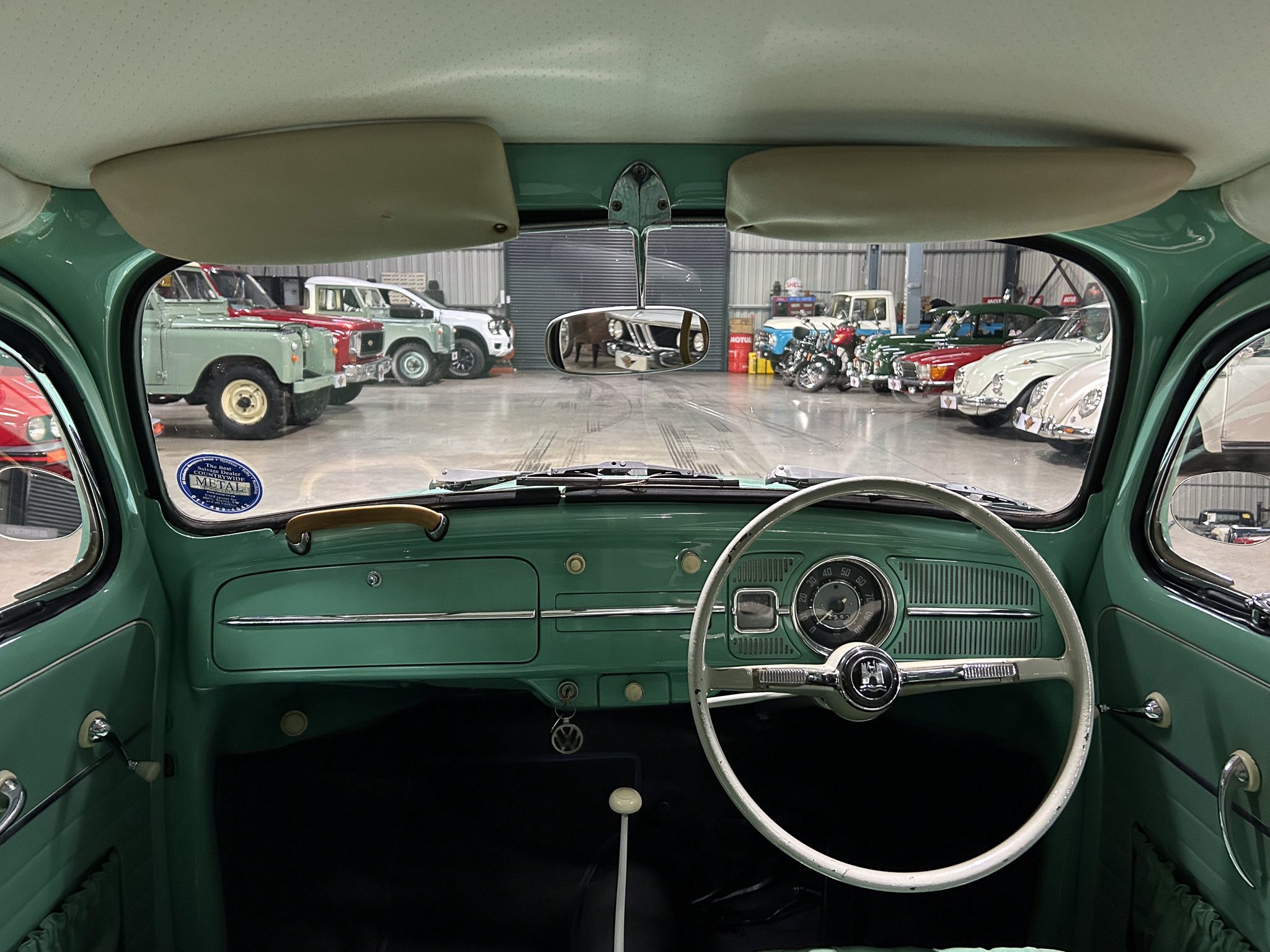 Inside a green vintage car, looking out onto a showroom filled with classic cars.