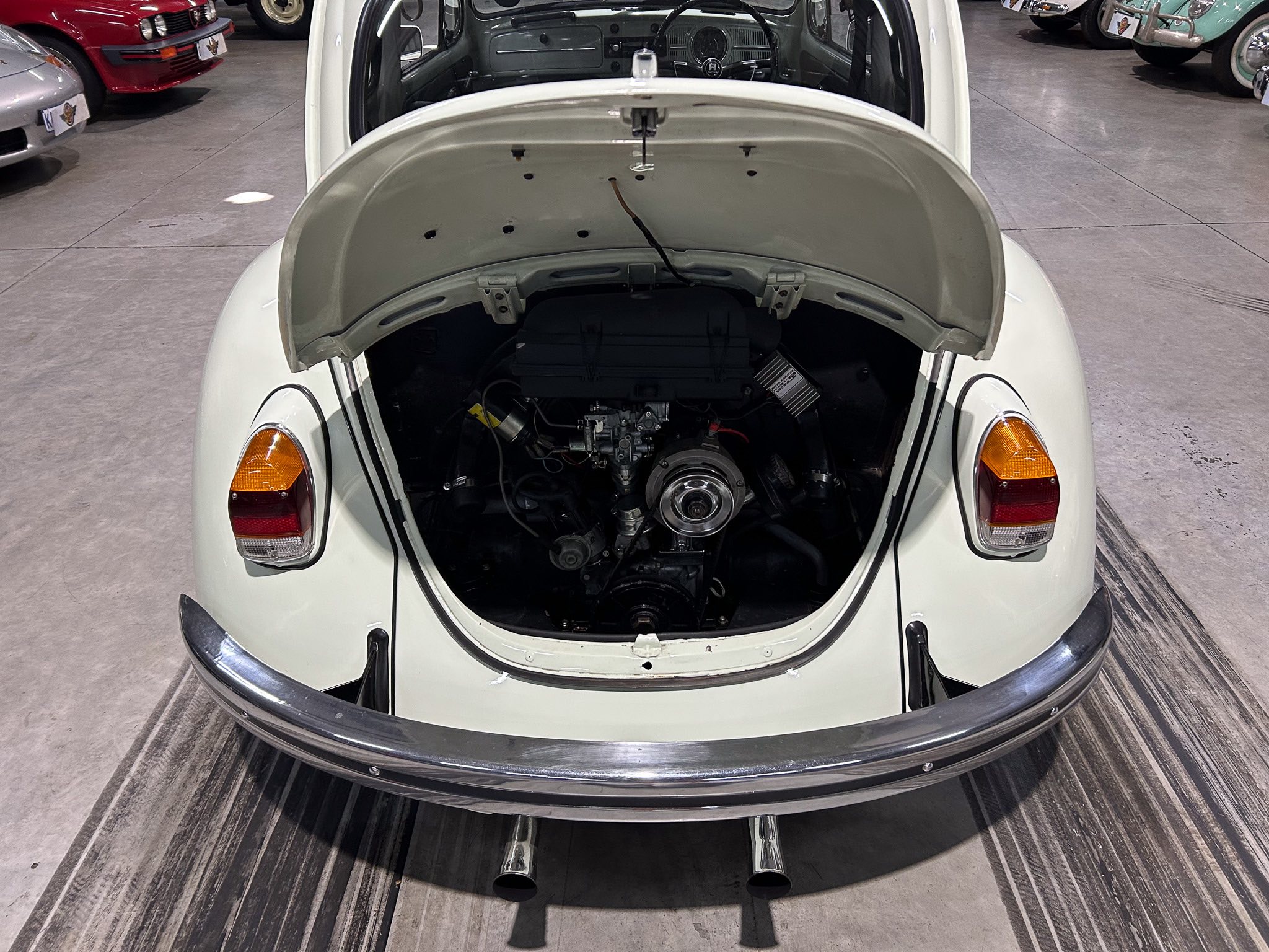 Open rear engine compartment of a white vintage car in a showroom, exposing the engine and exhaust pipes.