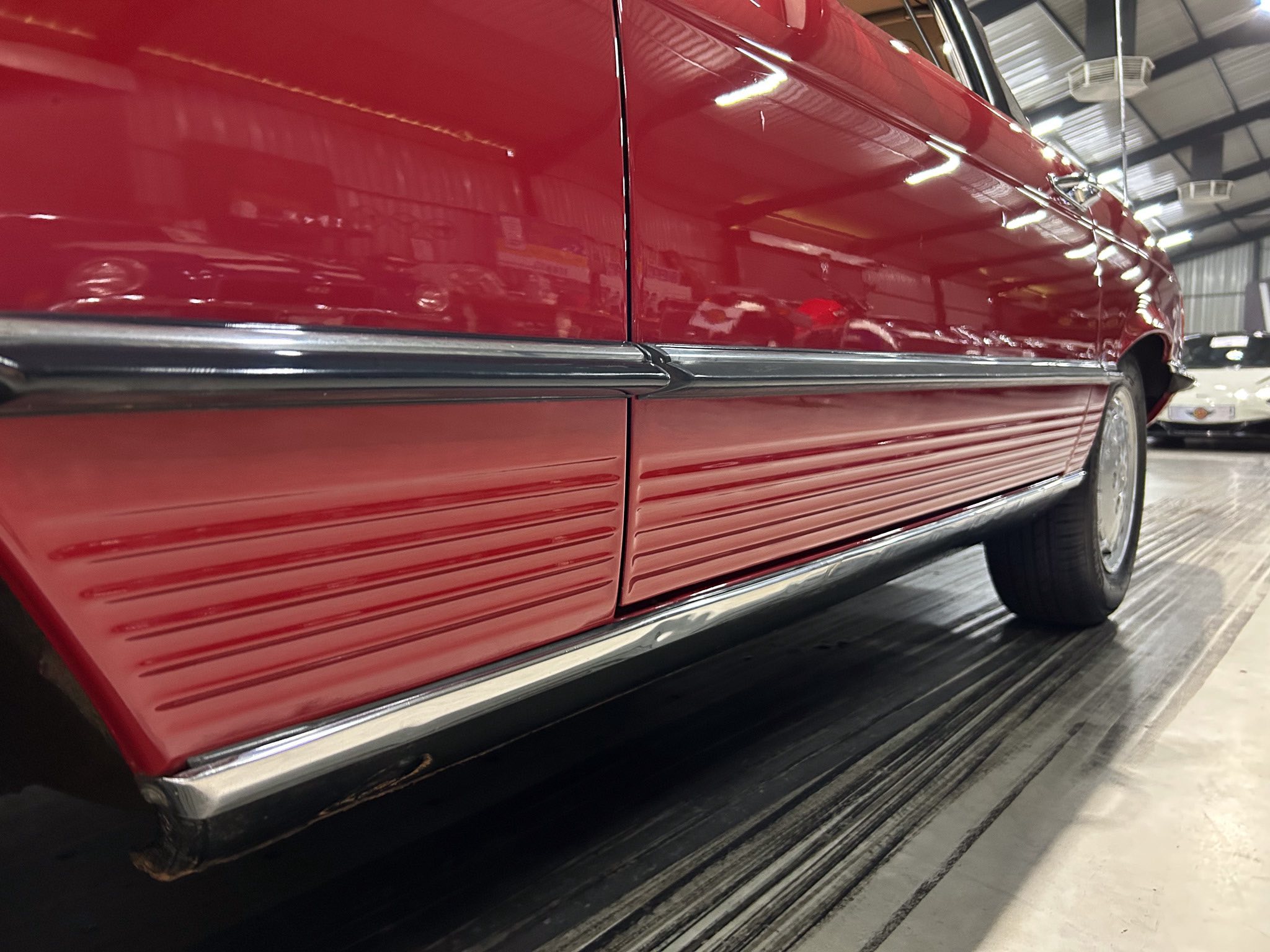 Close-up of a red vintage car door with chrome trim in a showroom, wheel visible at the back.