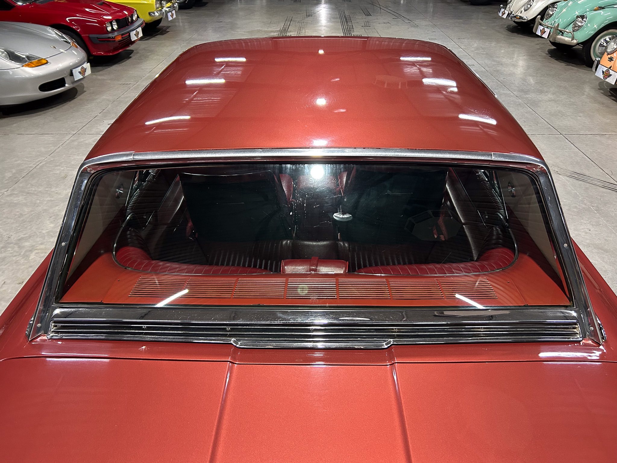 Top-down view of a red car hood in a showroom, surrounded by colorful classic cars on both sides.