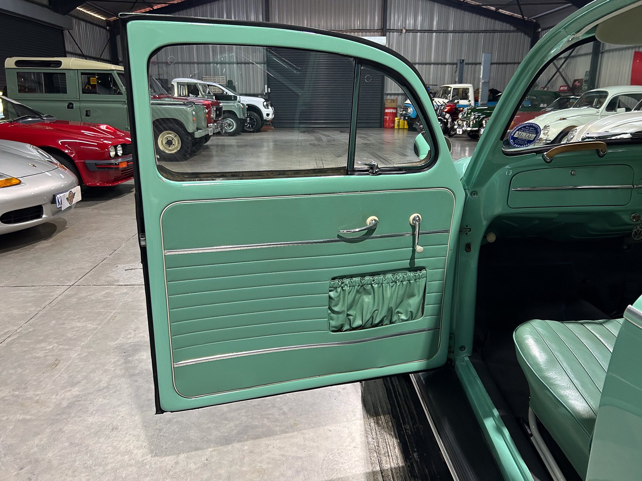 Open mint-green vintage car door revealing interior with chrome handles, in a showroom filled with classic cars.