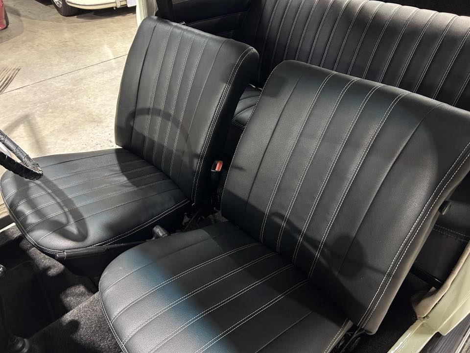 Black leather car seats with vertical white stitching in the front row of a vehicle, showing the driver and passenger seats.