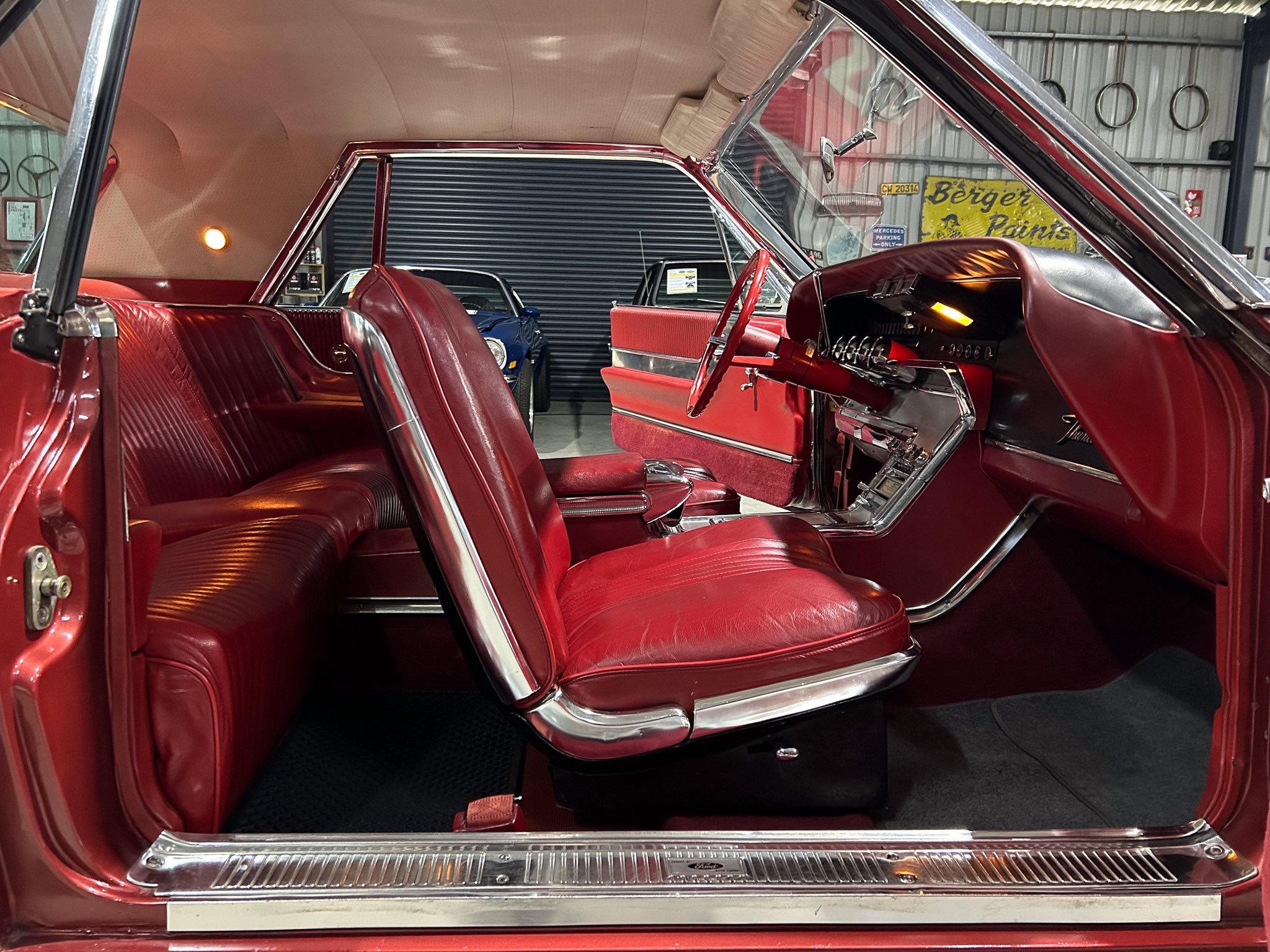 Interior of a vintage red car with burgundy leather seats and chrome trim, doors open in a showroom.