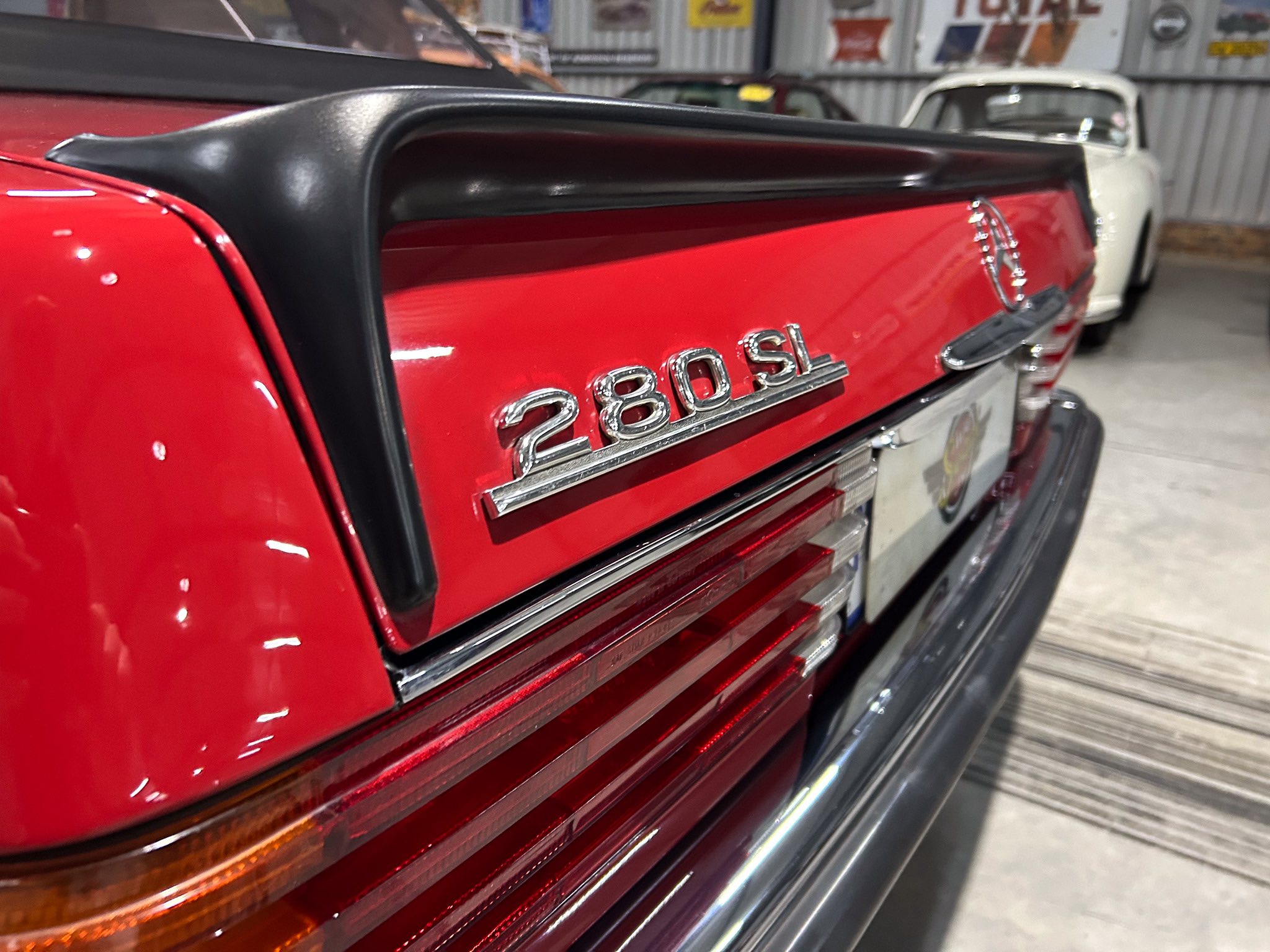 Rear view of a red Mercedes 280SL with the black soft-top stowed, chrome badge and taillight accents visible in a showroom.