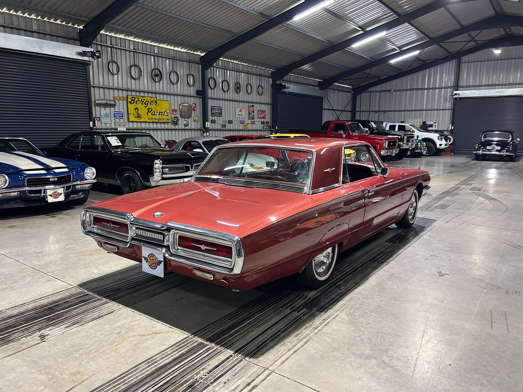 Interior view of a metal-walled garage filled with classic cars, red convertible in the foreground.