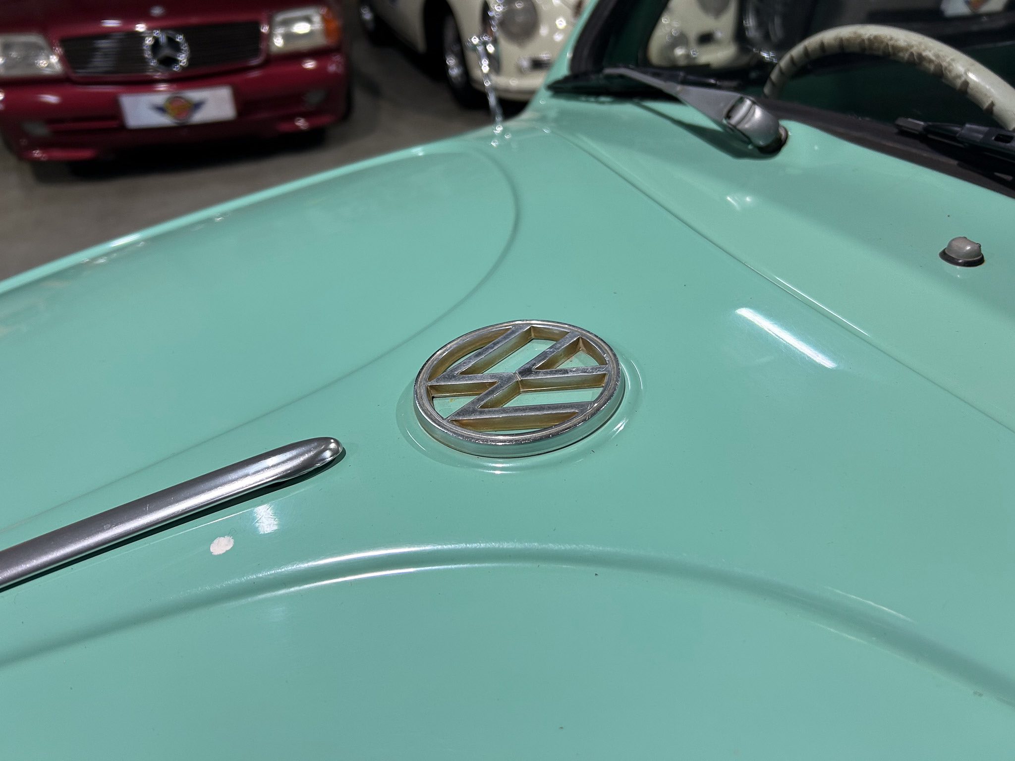 Close-up of a mint-green car hood with a VW emblem and windshield wipers in a showroom.