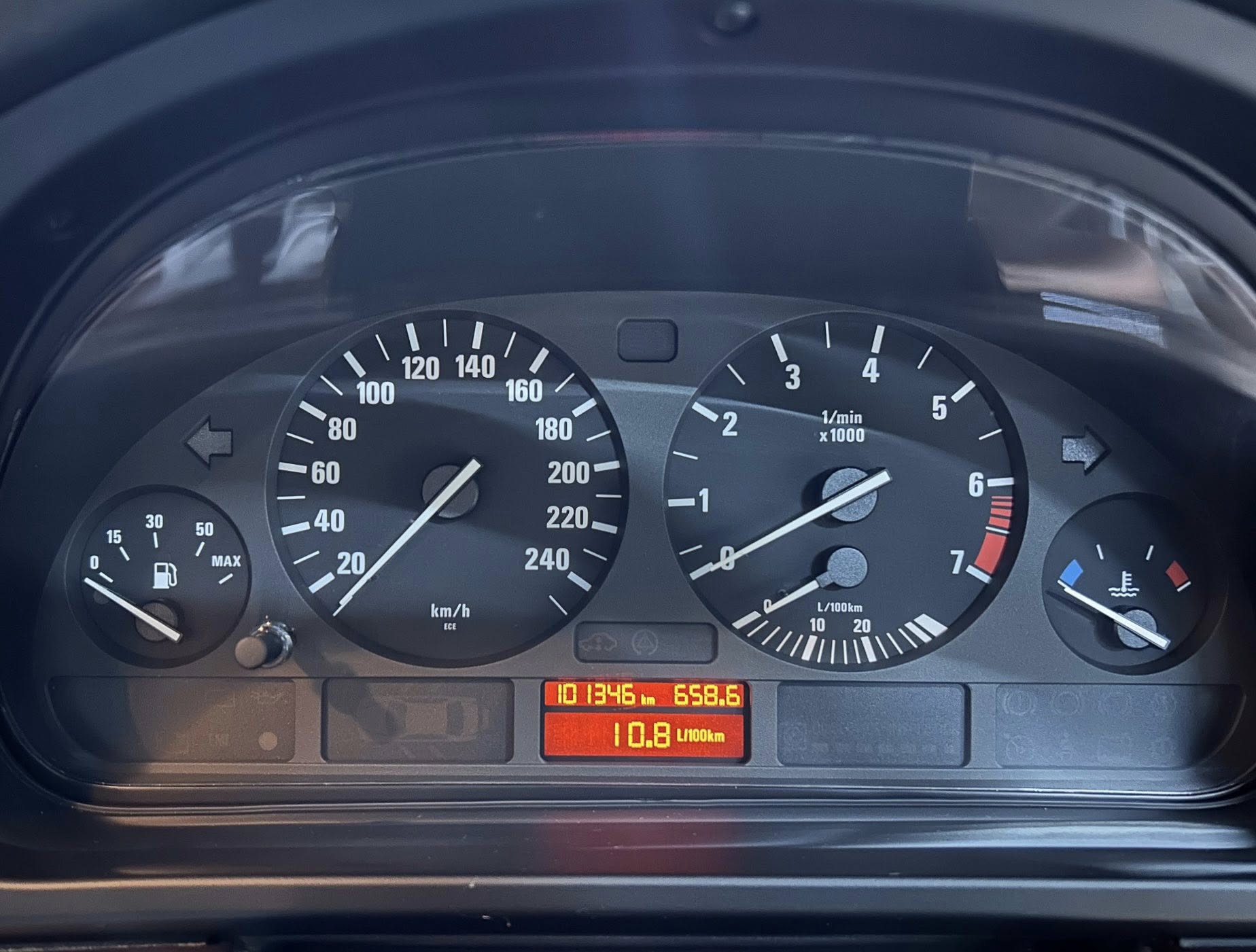Close-up of a car dashboard showing a speedometer (0–260 km/h) and tachometer, with a fuel gauge and digital readouts below.