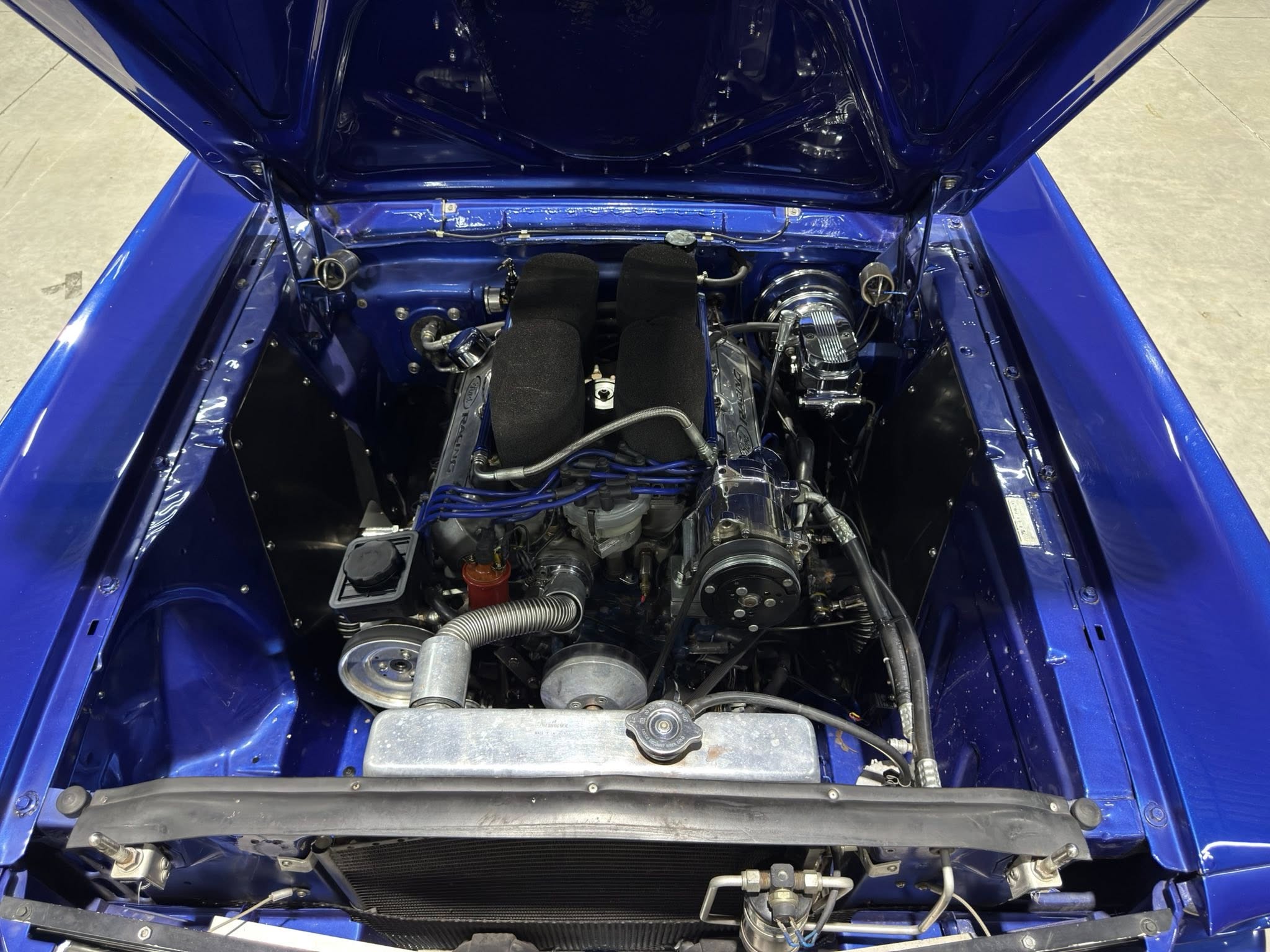 Open hood engine bay of a bright blue car, showing a detailed V-shaped engine with black foam air filters and chrome components in the center.