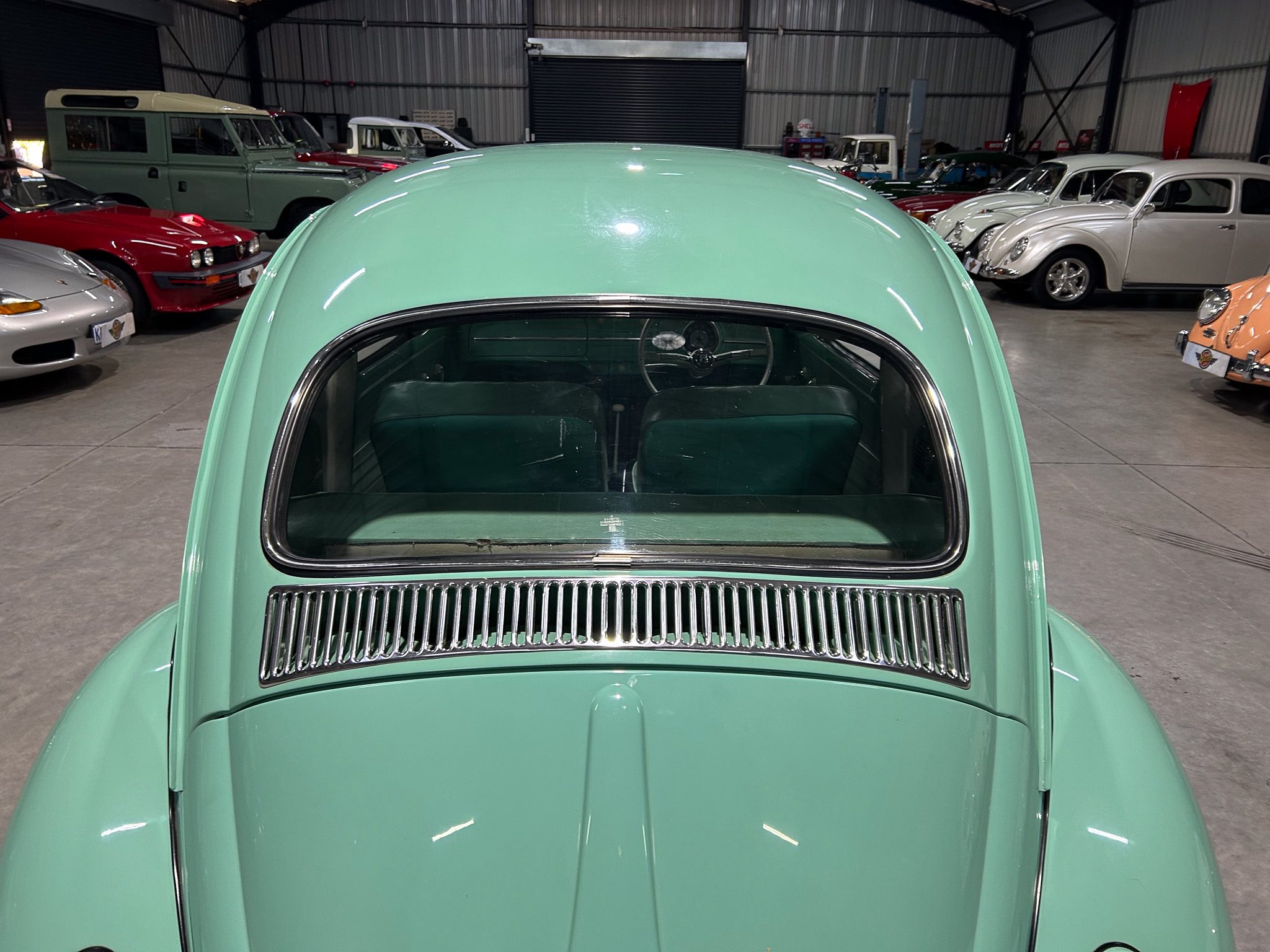 Front view of a mint-green vintage car with its rounded hood in a large showroom filled with classic cars.
