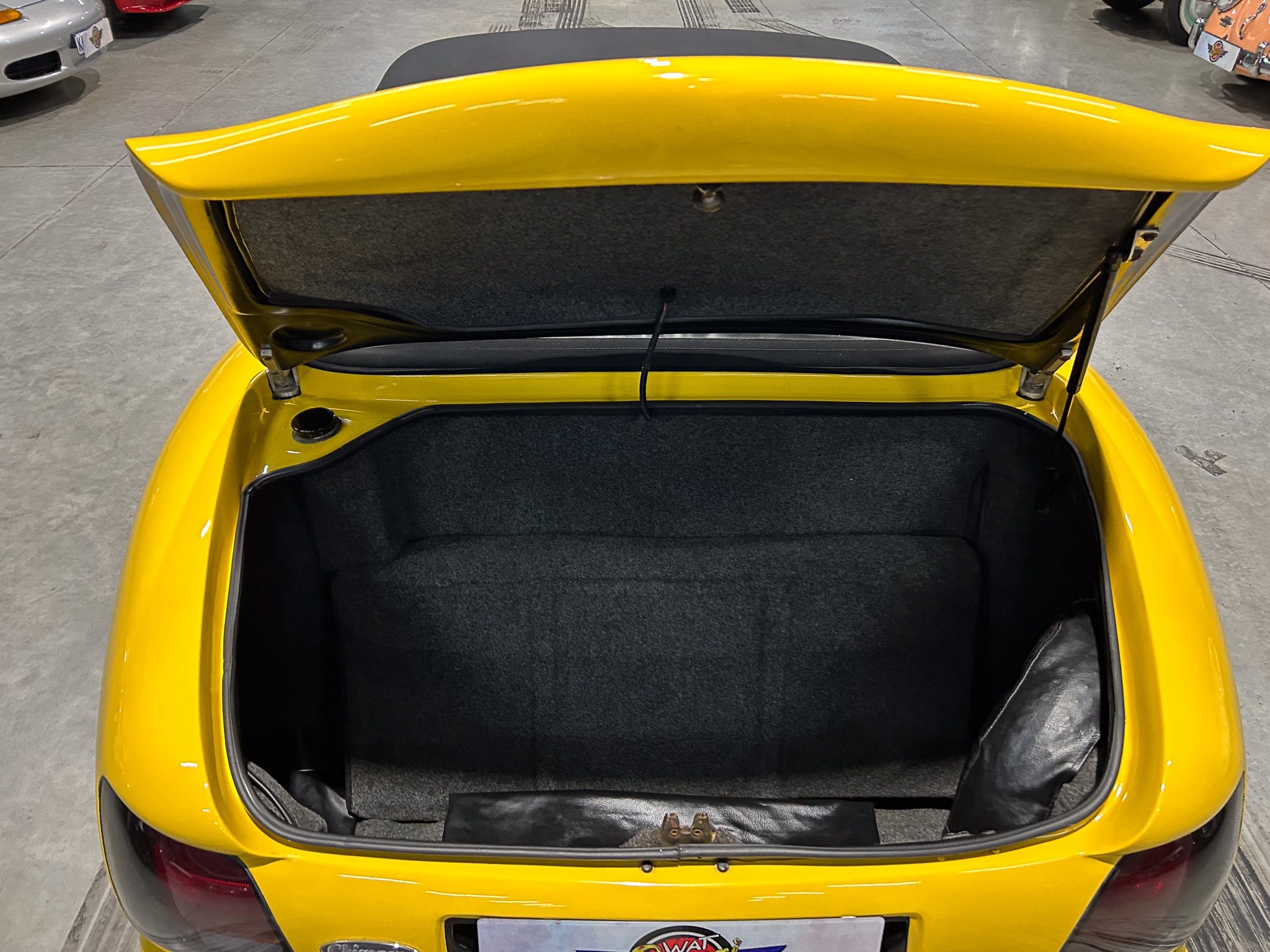 Open yellow car trunk showing dark interior and luggage space in a showroom.