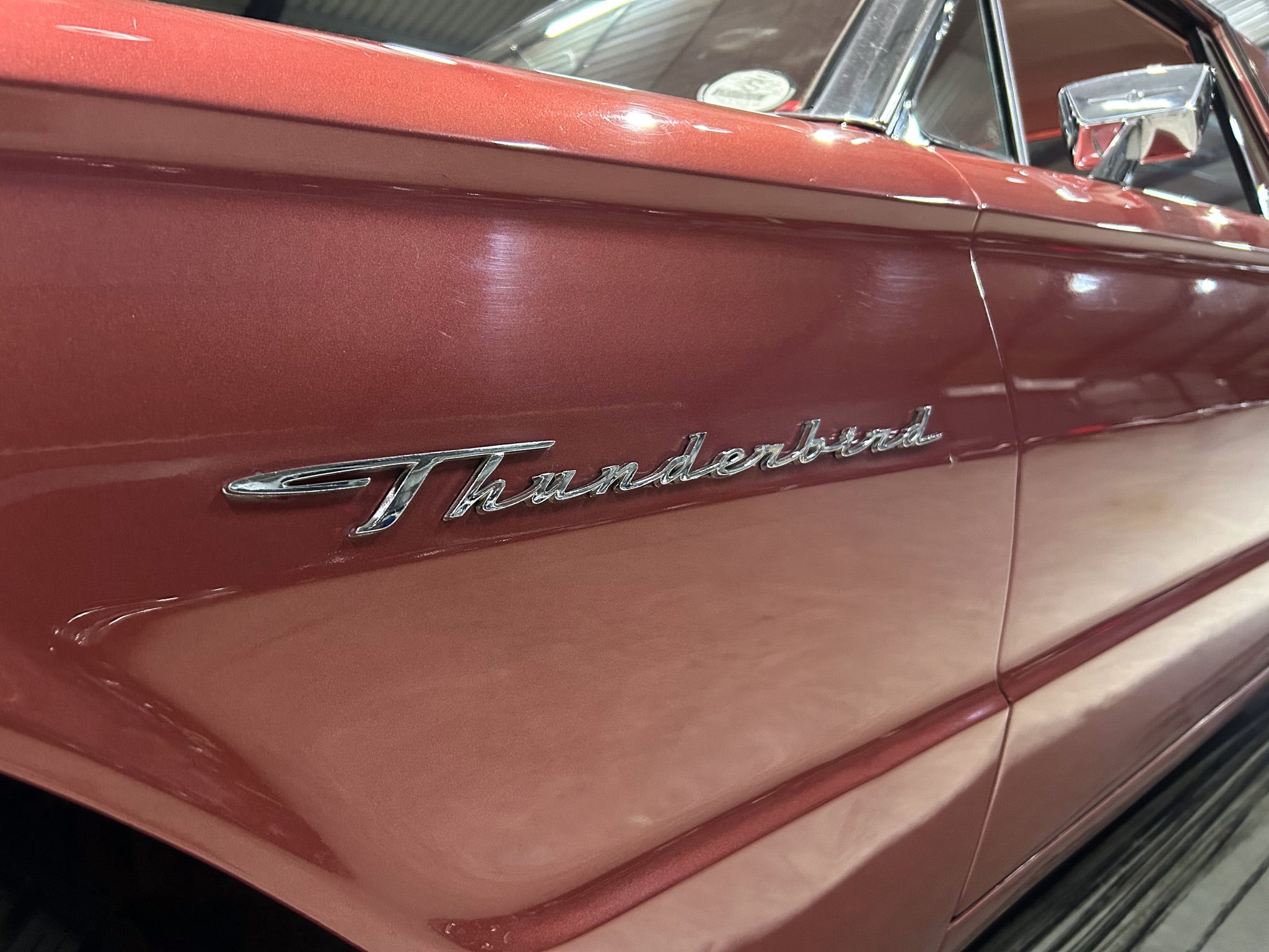 Close-up of a maroon car door with chrome Thunderbird script badge visible along the lower panel