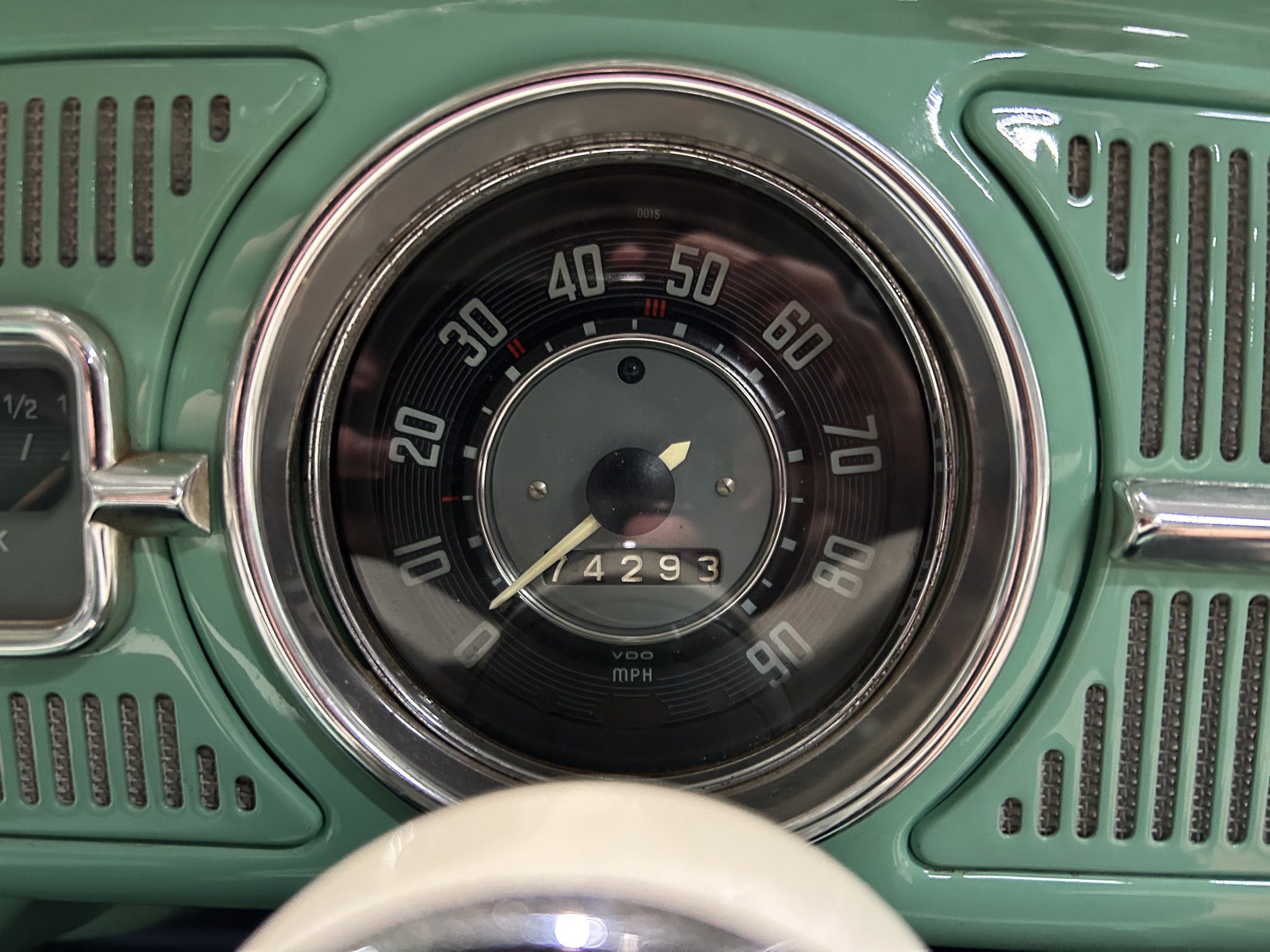 Close-up of a vintage car dashboard with a circular speedometer up to 90 mph, chrome bezel, and a numbered odometer reading 14293, set in a green panel.