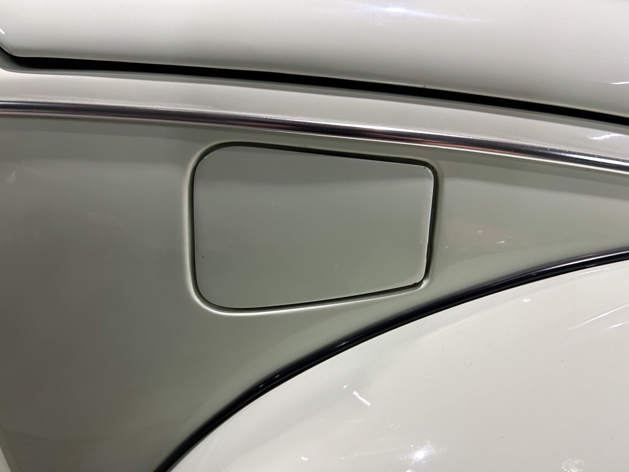 Close-up of a silver car's fuel filler door with surrounding body panel and chrome trim.