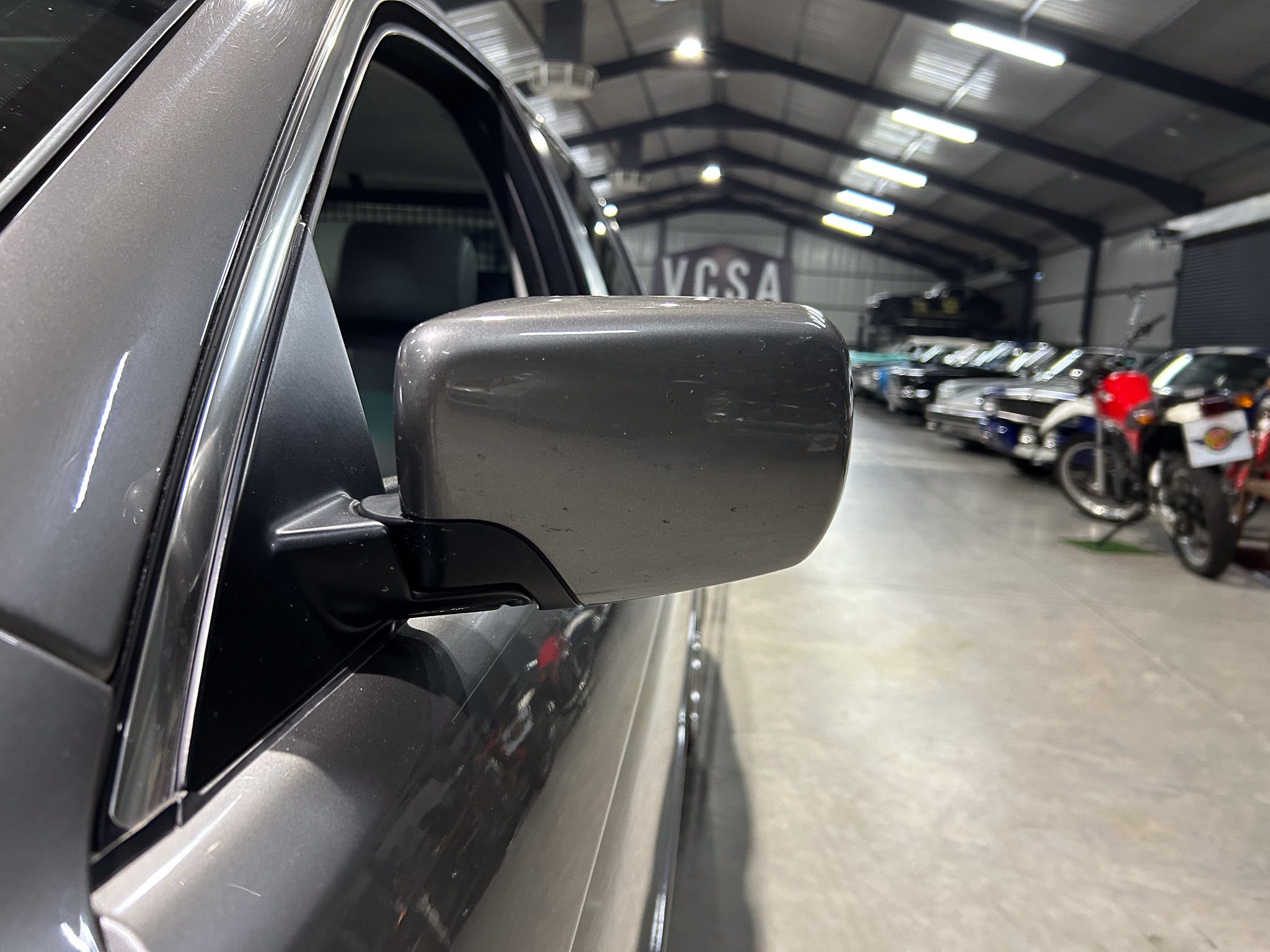 Close-up of a gray car side mirror on a vehicle inside a bright showroom with other cars in the background