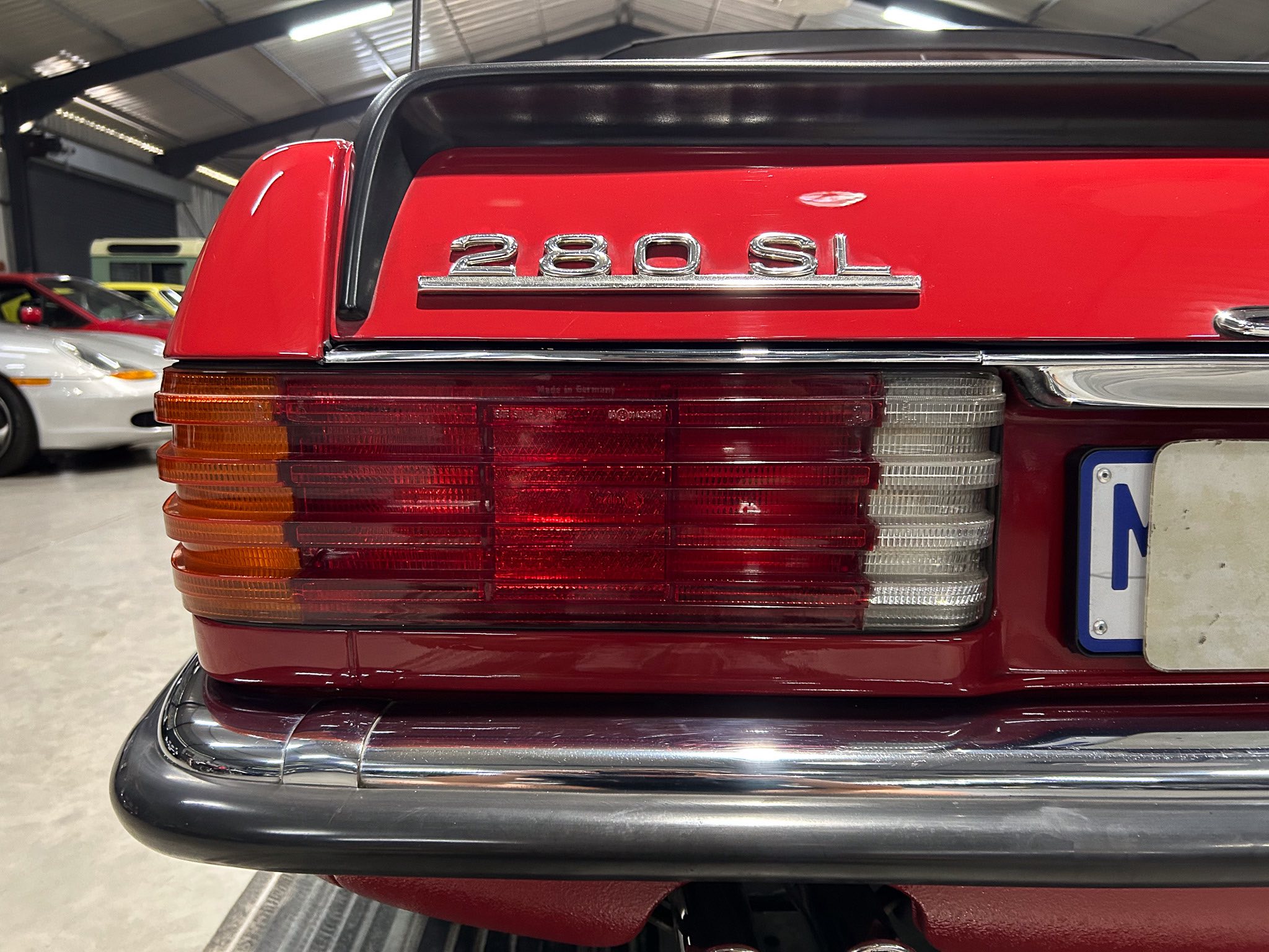 Rear of a red vintage Mercedes 280SL with chrome badge and tail lights in a showroom setting