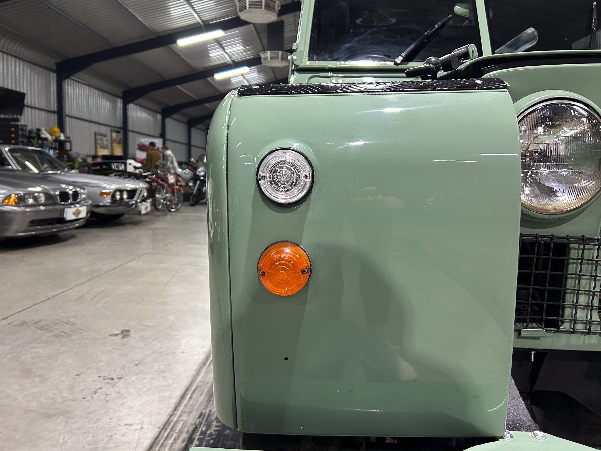 Close-up of a mint-green vehicle's front panel with a round headlight and orange turn signal in a workshop.