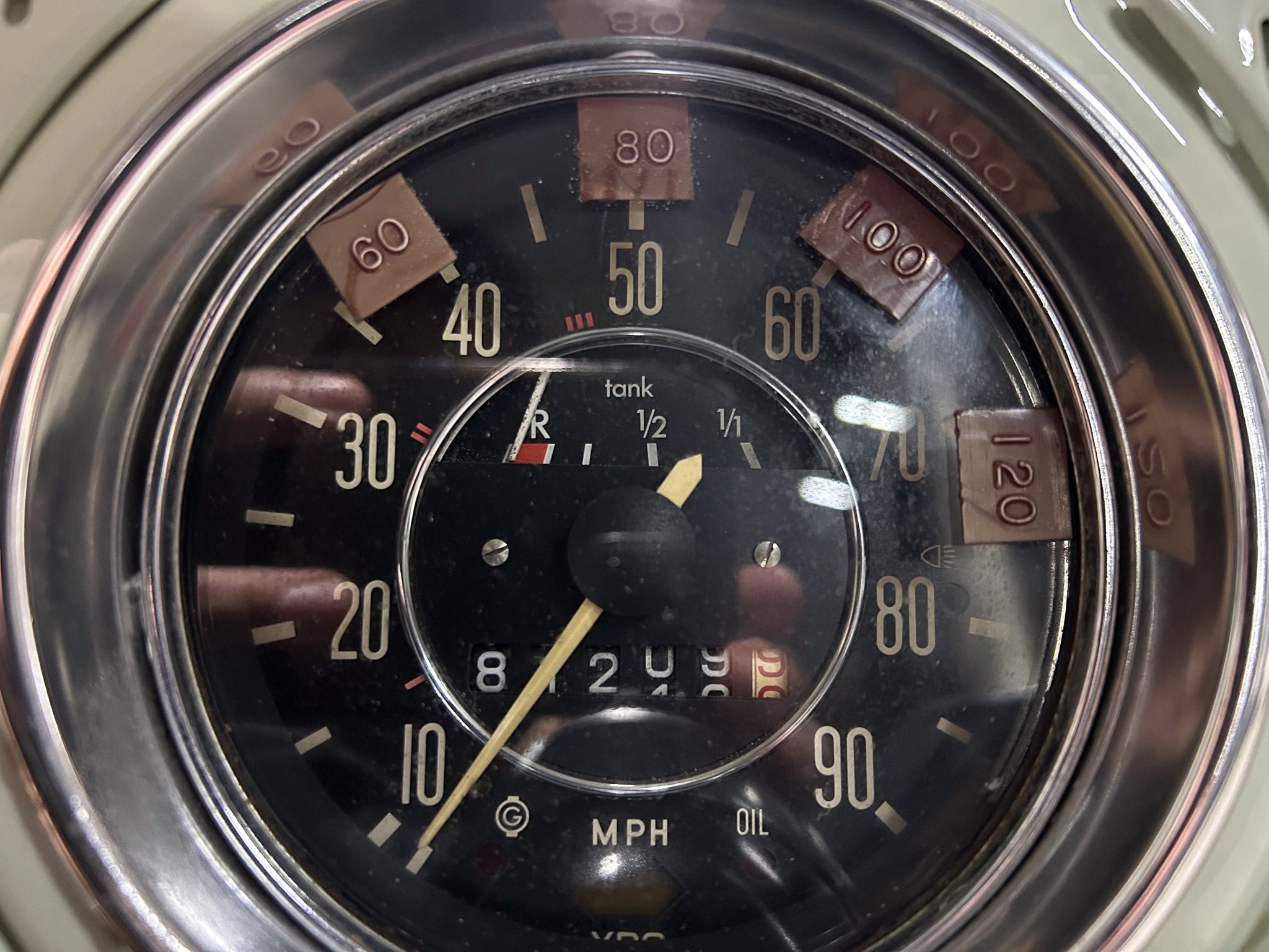 Close-up of a vintage car speedometer showing mph with the needle near 0, chrome bezel around the dial.