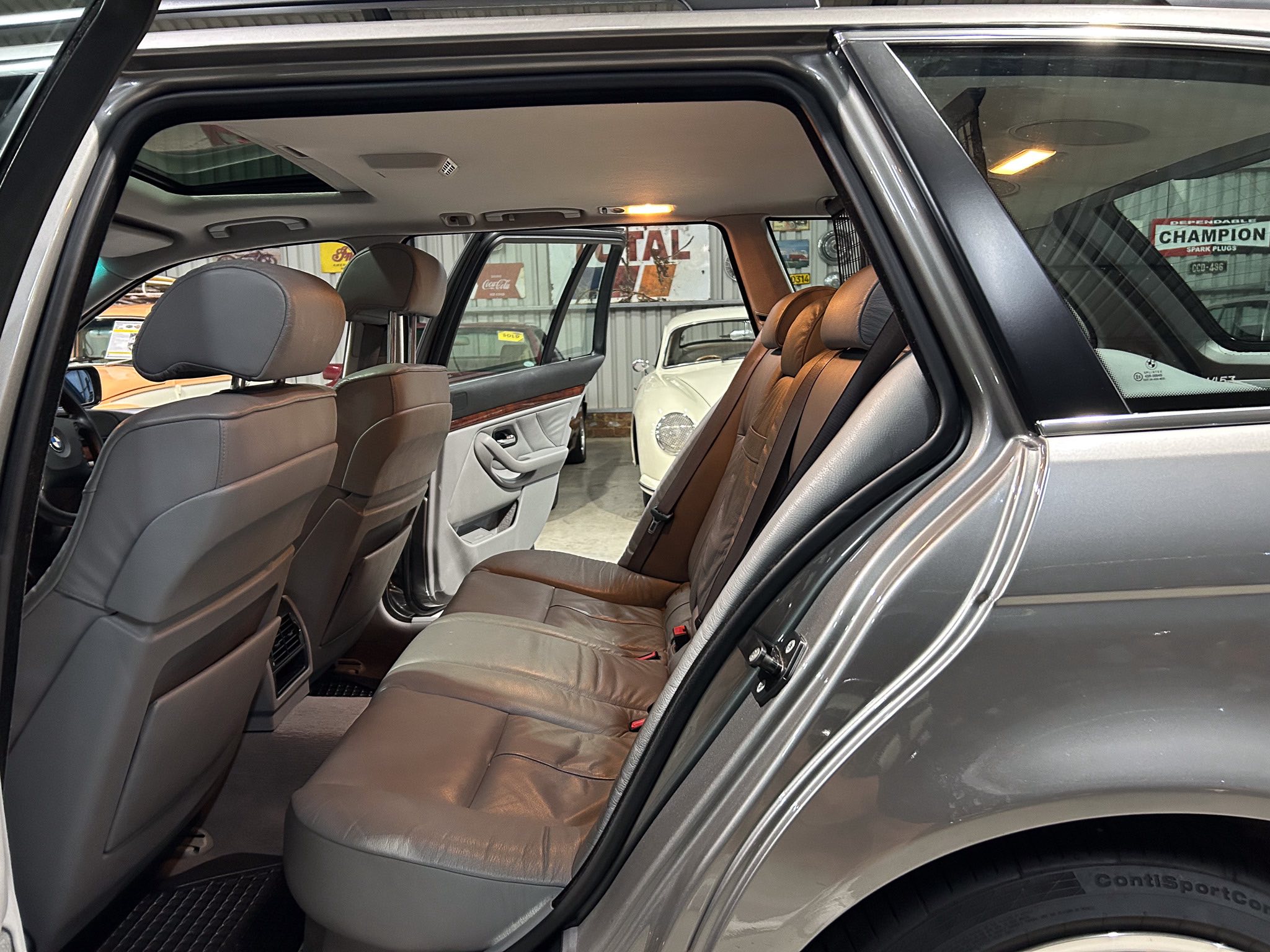 Rear passenger area of a gray SUV with tan leather seats; doors open showing a showroom with classic cars in the background
