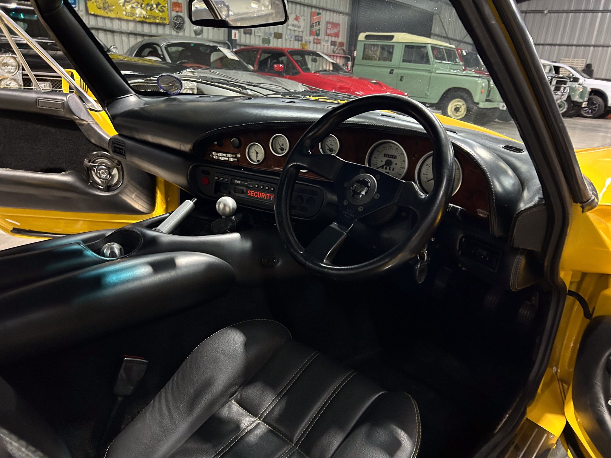 Interior view of a yellow car showing the black dashboard, steering wheel, and leather seats from the driver’s seat angle in a showroom.
