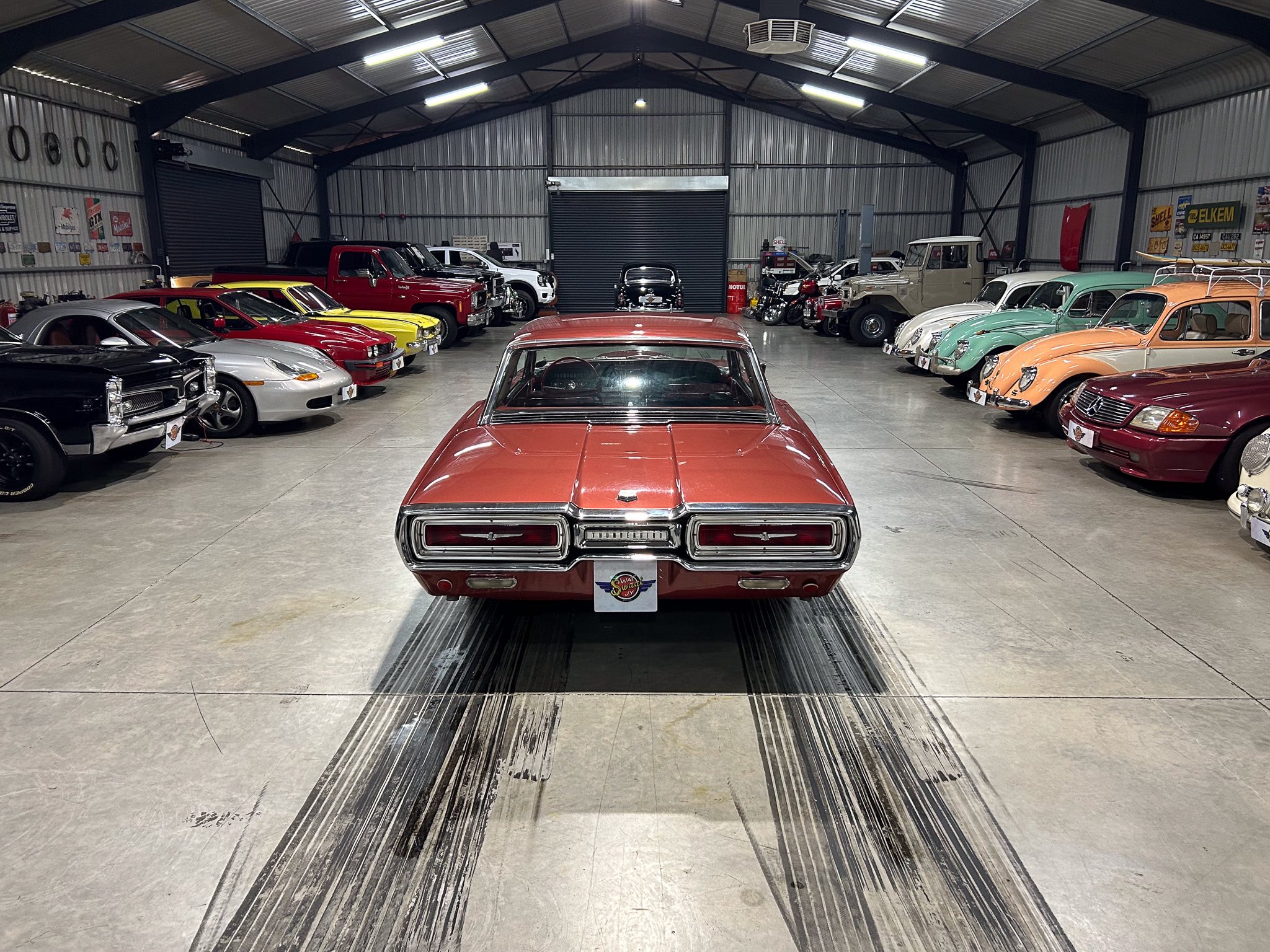 Interior of a vintage car showroom with rows of classic cars along both walls and a red car centered in the foreground as the focal point.