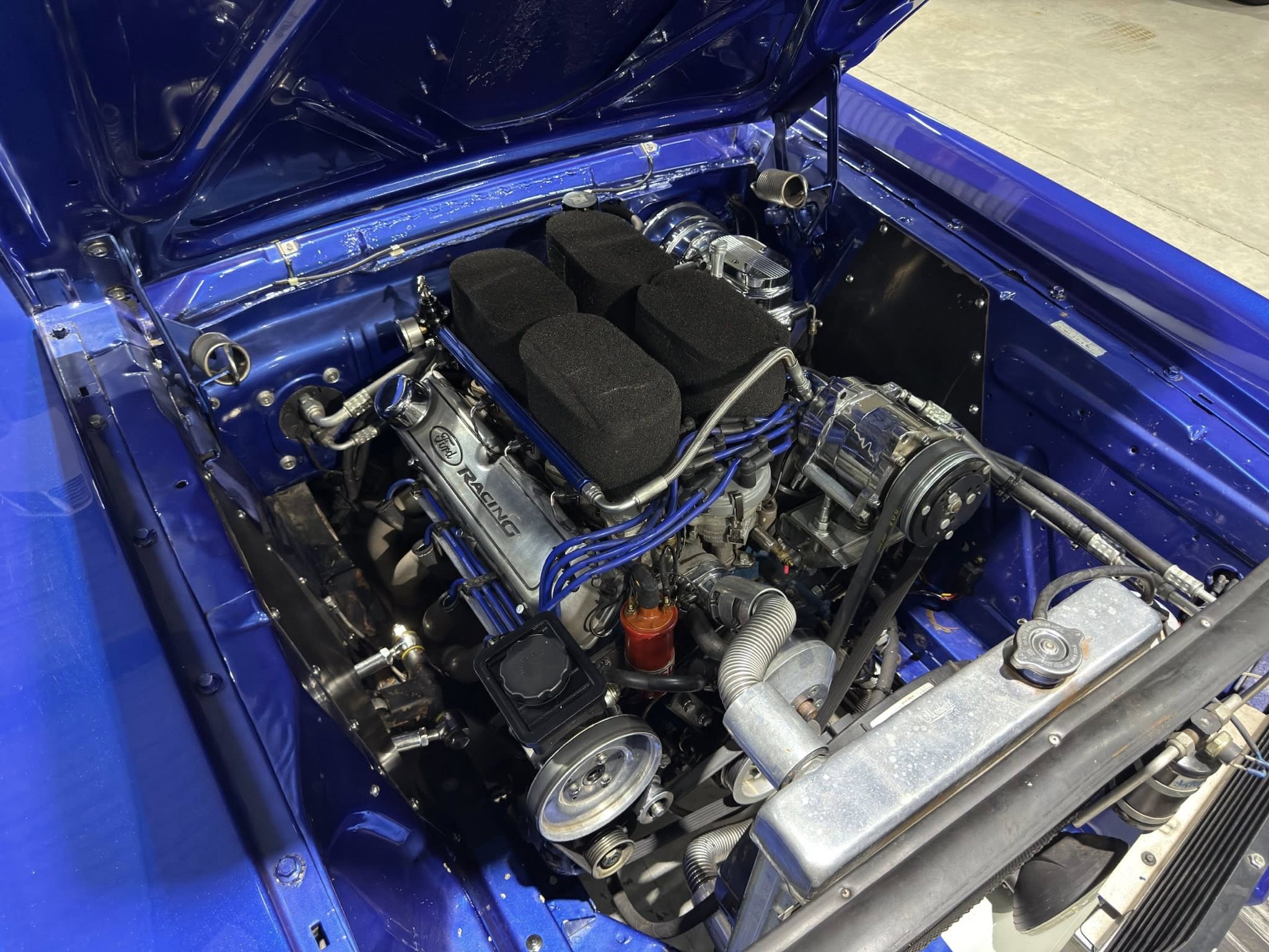 Blue race car engine bay with chrome intake, black foam air filters, and blue wiring visible under the open hood