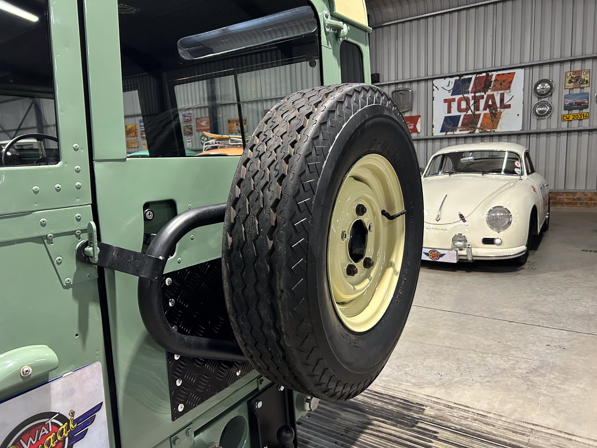 Close-up of a spare tire mounted on the side of a green vintage military-style vehicle inside a showroom or garage.