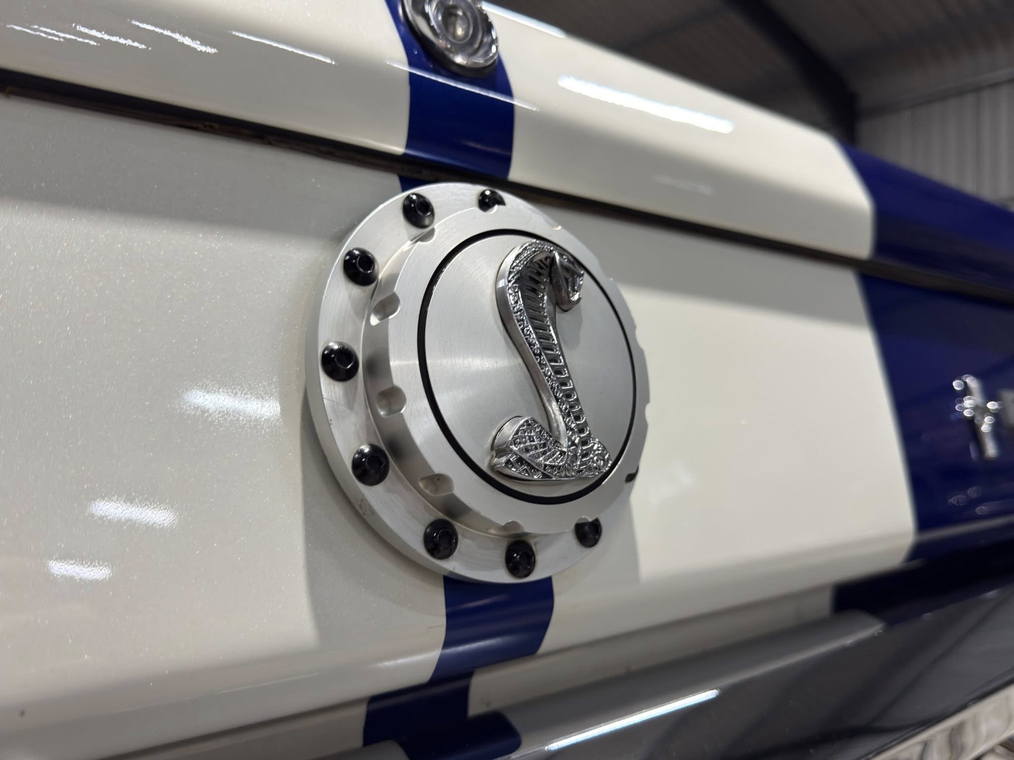 Close-up of a silver circular access cover with multiple bolts on a white panel with a blue stripe.