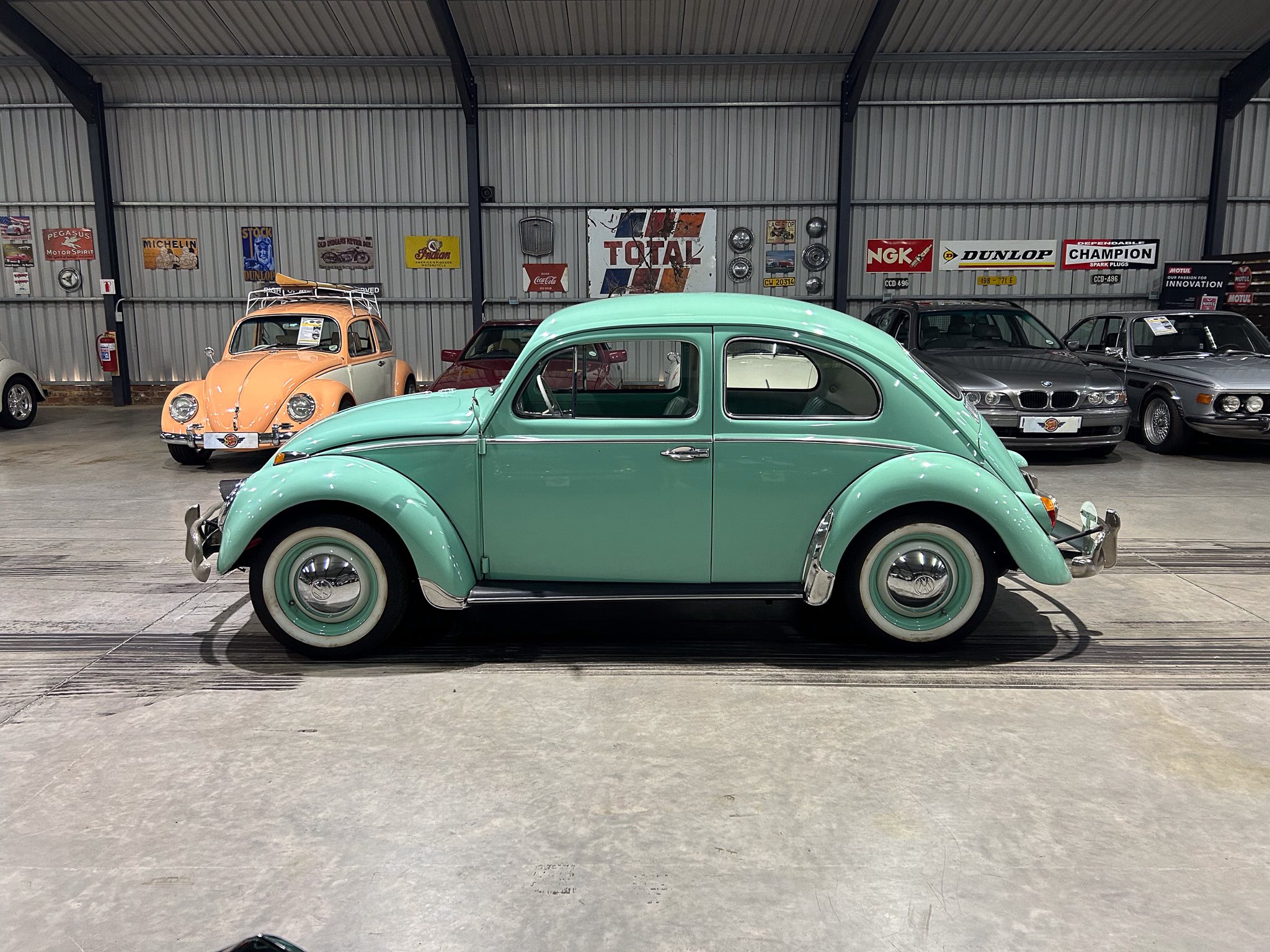 Mint green vintage car in a showroom with other classic cars and retro wall signs in the background.