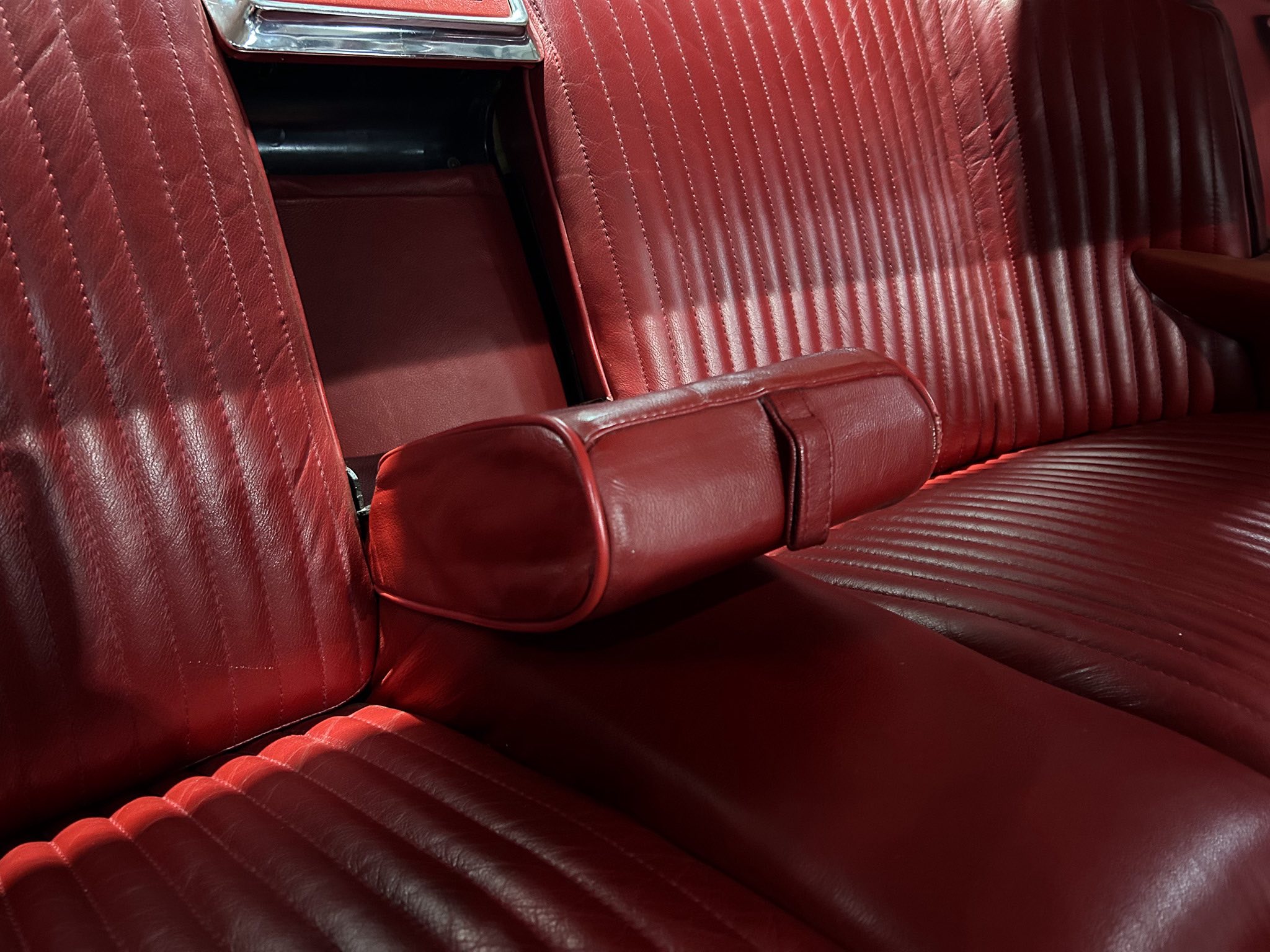 Close-up of red leather car seats with vertical stitching and a central armrest visible between seats.