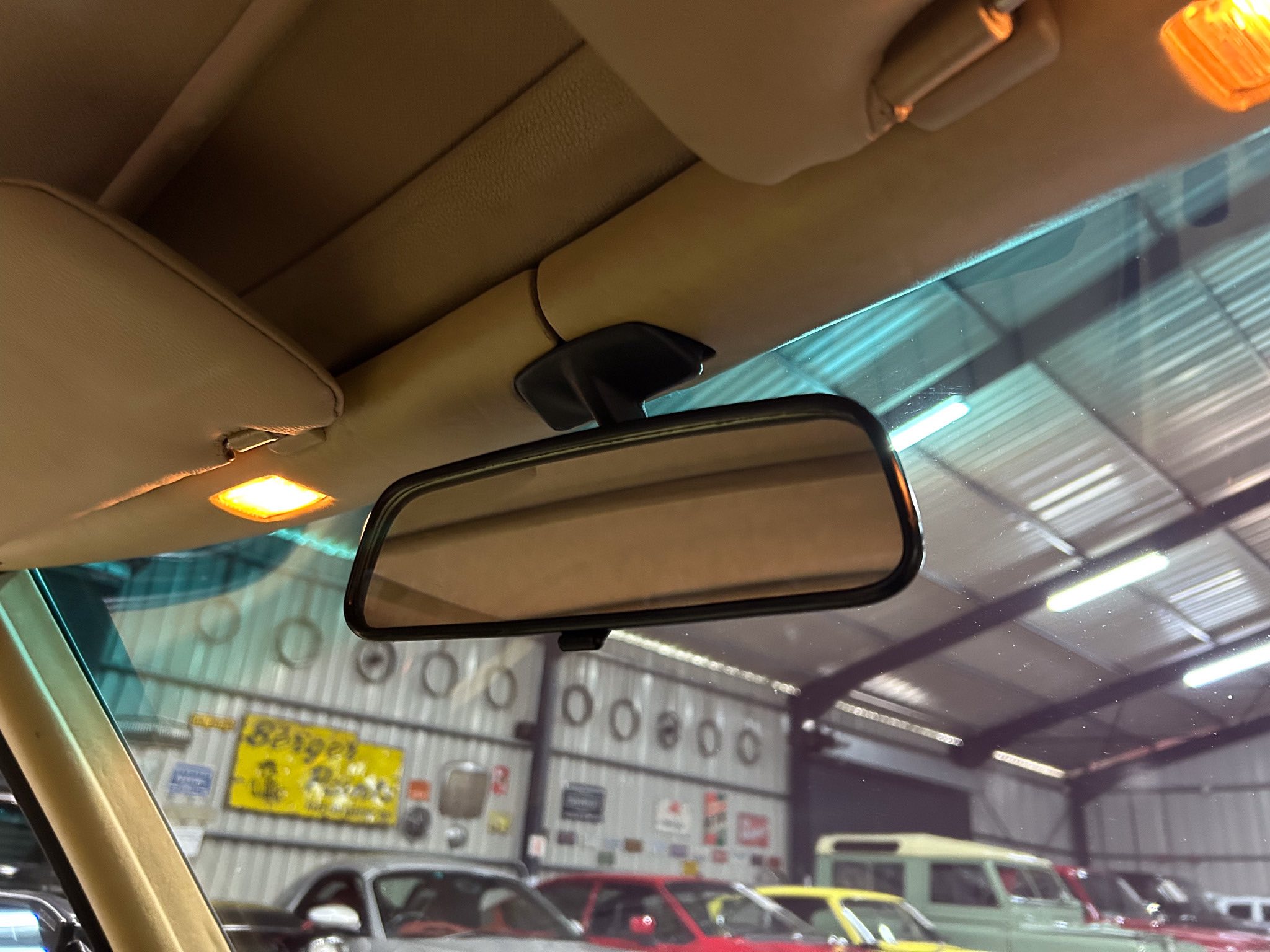 Tan car interior with rearview mirror and orange overhead light visible through the windshield, as seen in a showroom or garage.