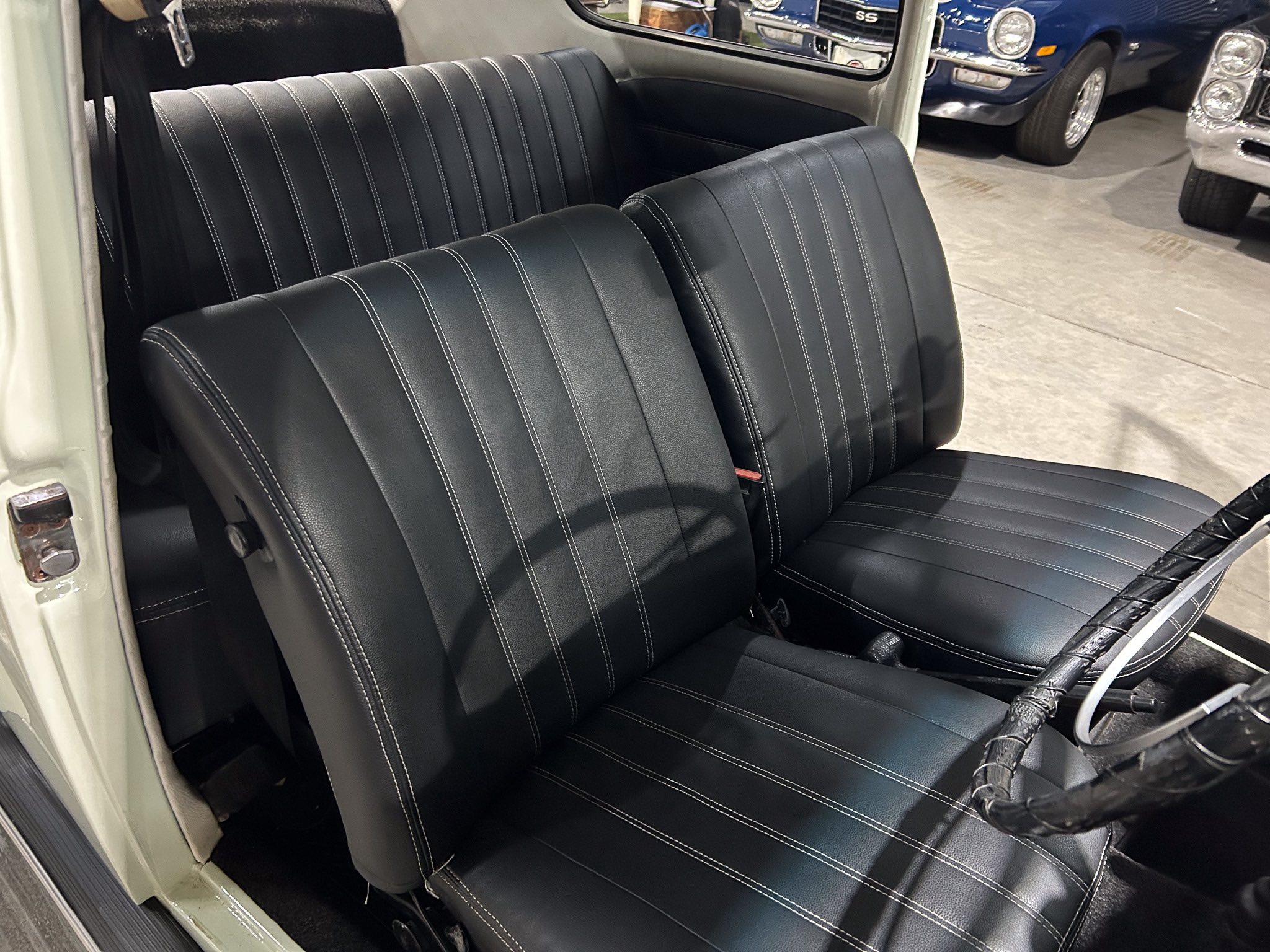 Black leather car seats with white contrast stitching inside a vehicle, showing front and rear seating.