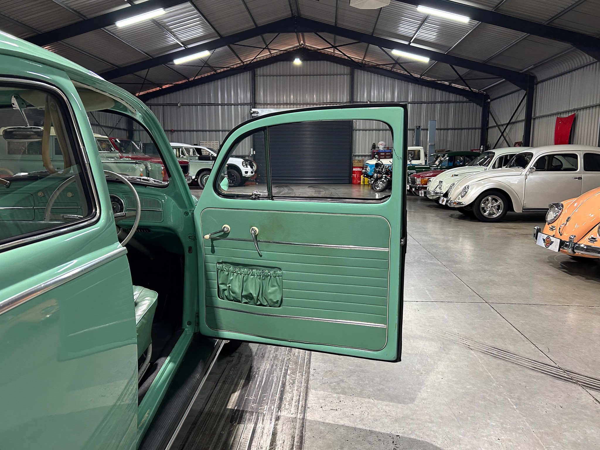 Open green vintage car door in a warehouse showroom with a line of classic cars parked inside.