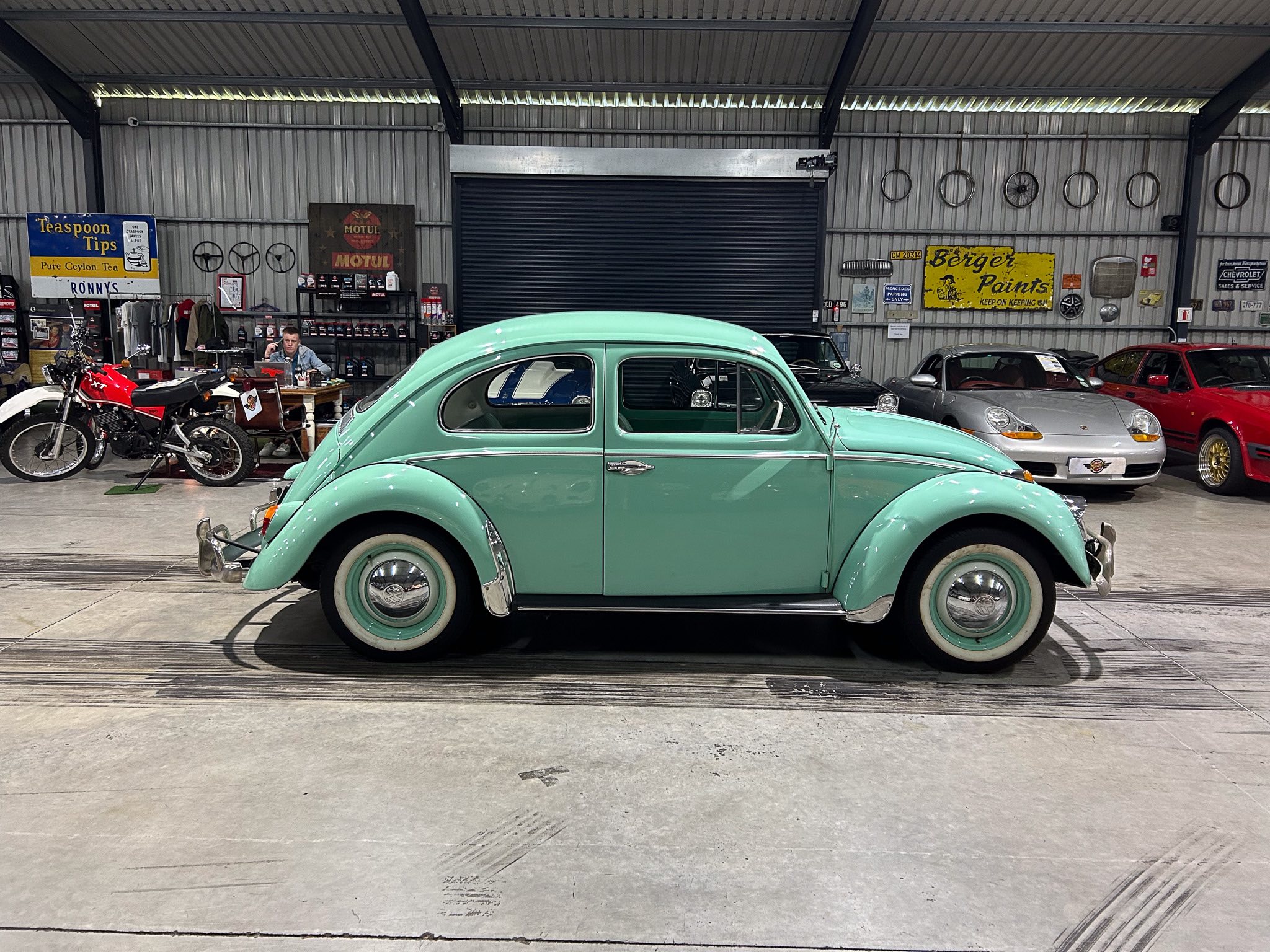 Mint green vintage car in a showroom with other classic cars and retro signs on the walls.