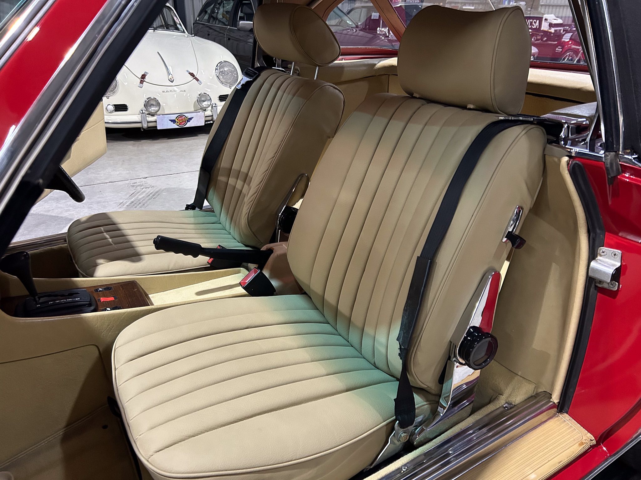 Beige leather car seats in a vintage red car, with a white classic car visible outside through the window.