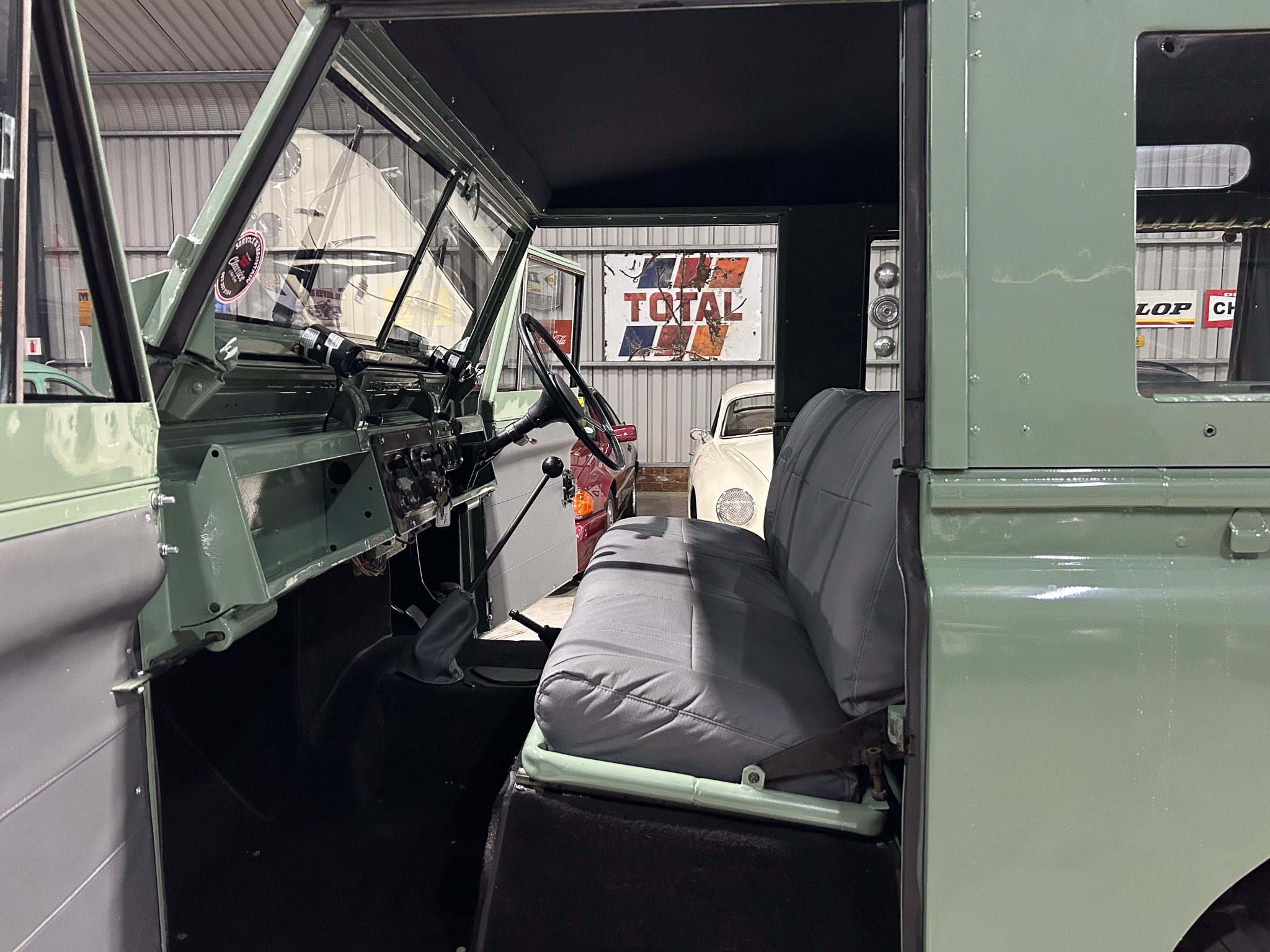 Interior of an olive-green military truck with steering wheel, dashboard, and front bench seat visible in the cabin.