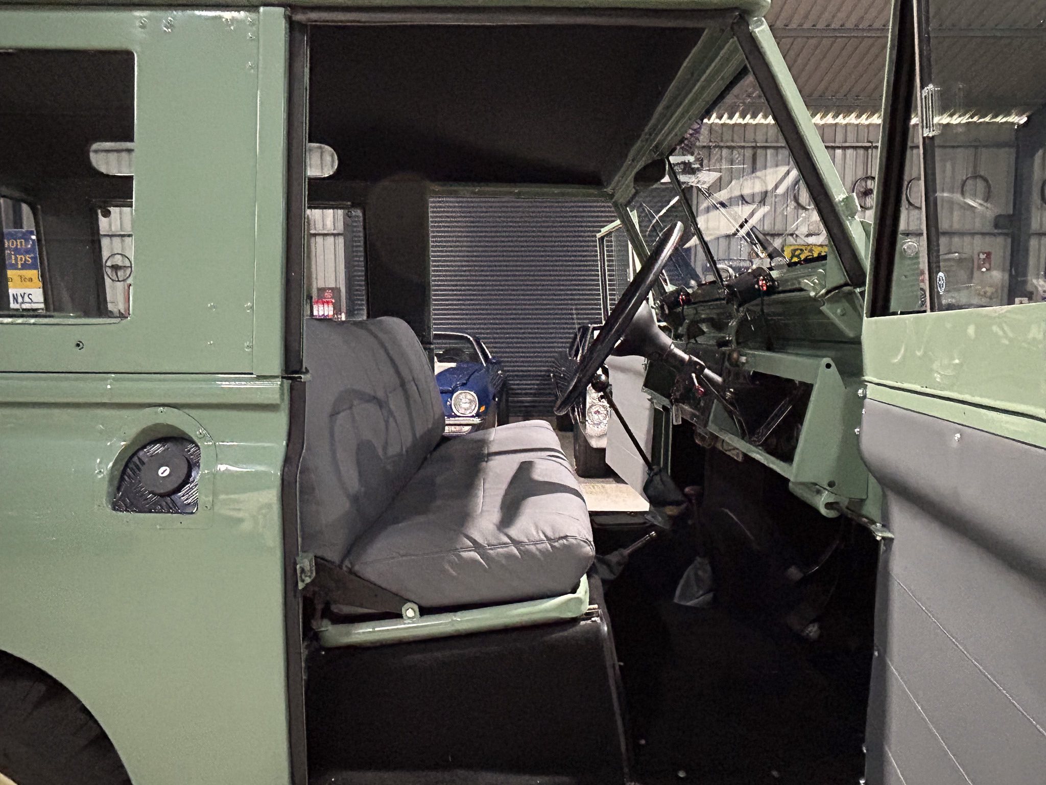 Interior of a green vehicle with a torn windshield, exposed metal, and a worn driver's seat in a dim garage.
